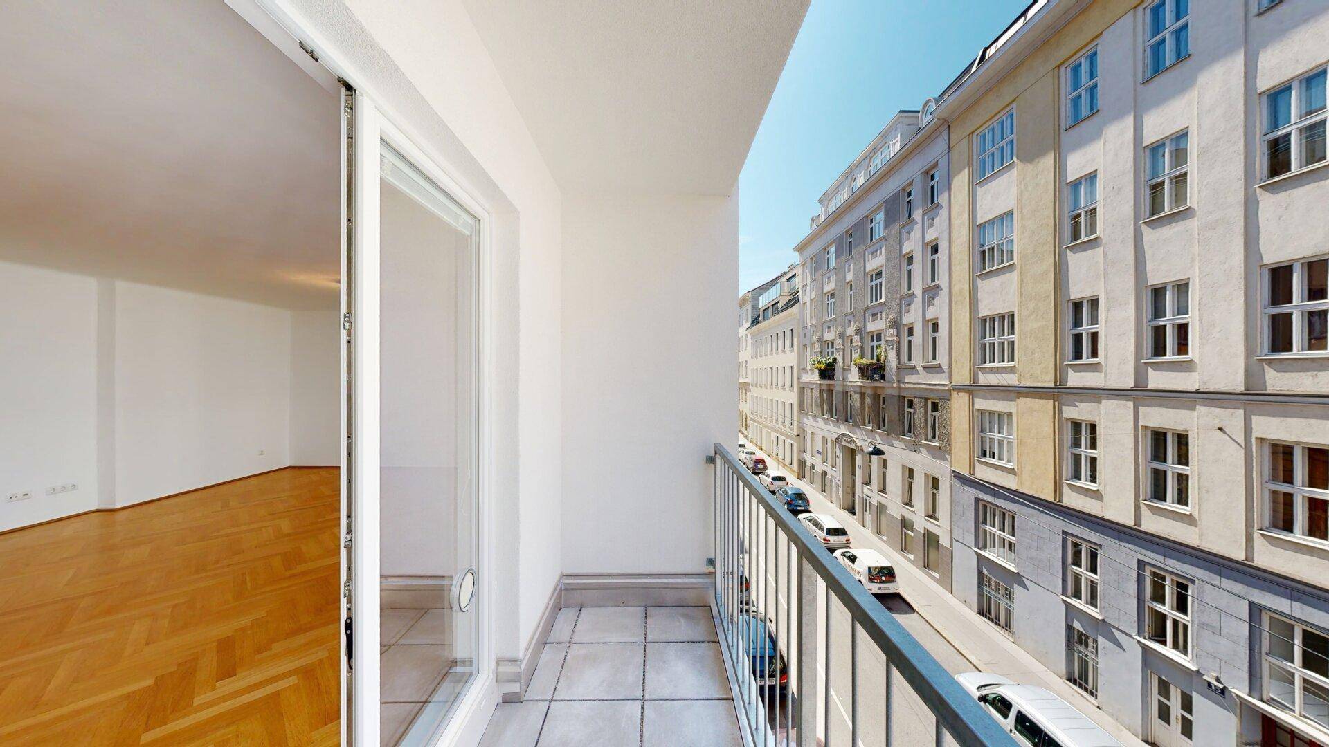 Kleiner Balkon mit Fliesenboden und Blick auf die belebte Stadtstraße.