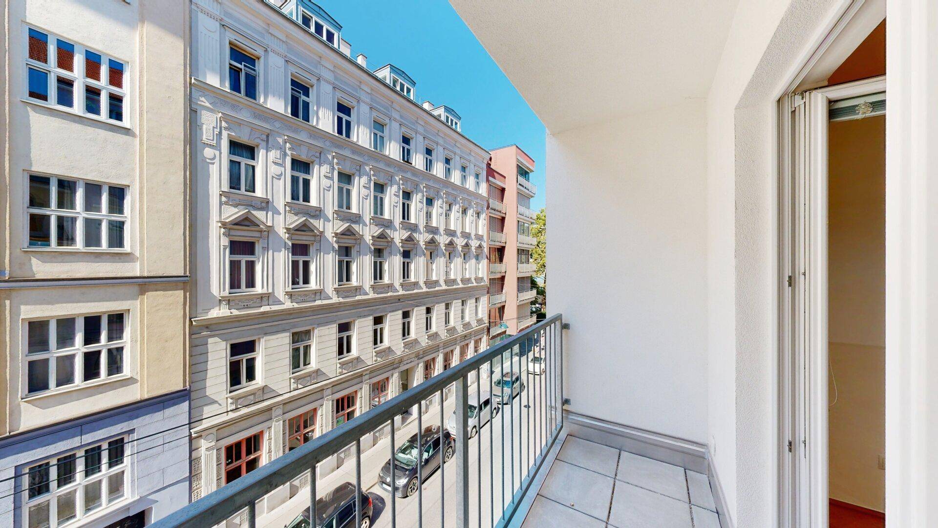 Balkon mit Metallgeländer und Blick auf die umliegenden Gebäude und die Straße.