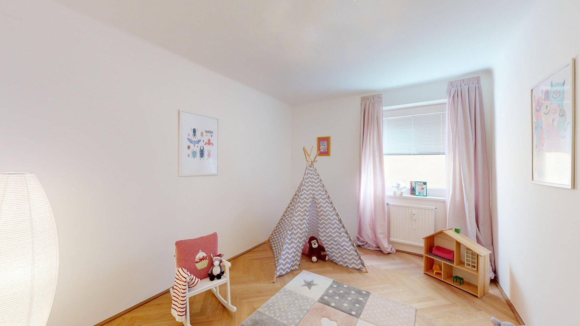 Freundliches Kinderzimmer mit Fischgrätparkett, Spielteppich und viel Tageslicht durch das Fenster.