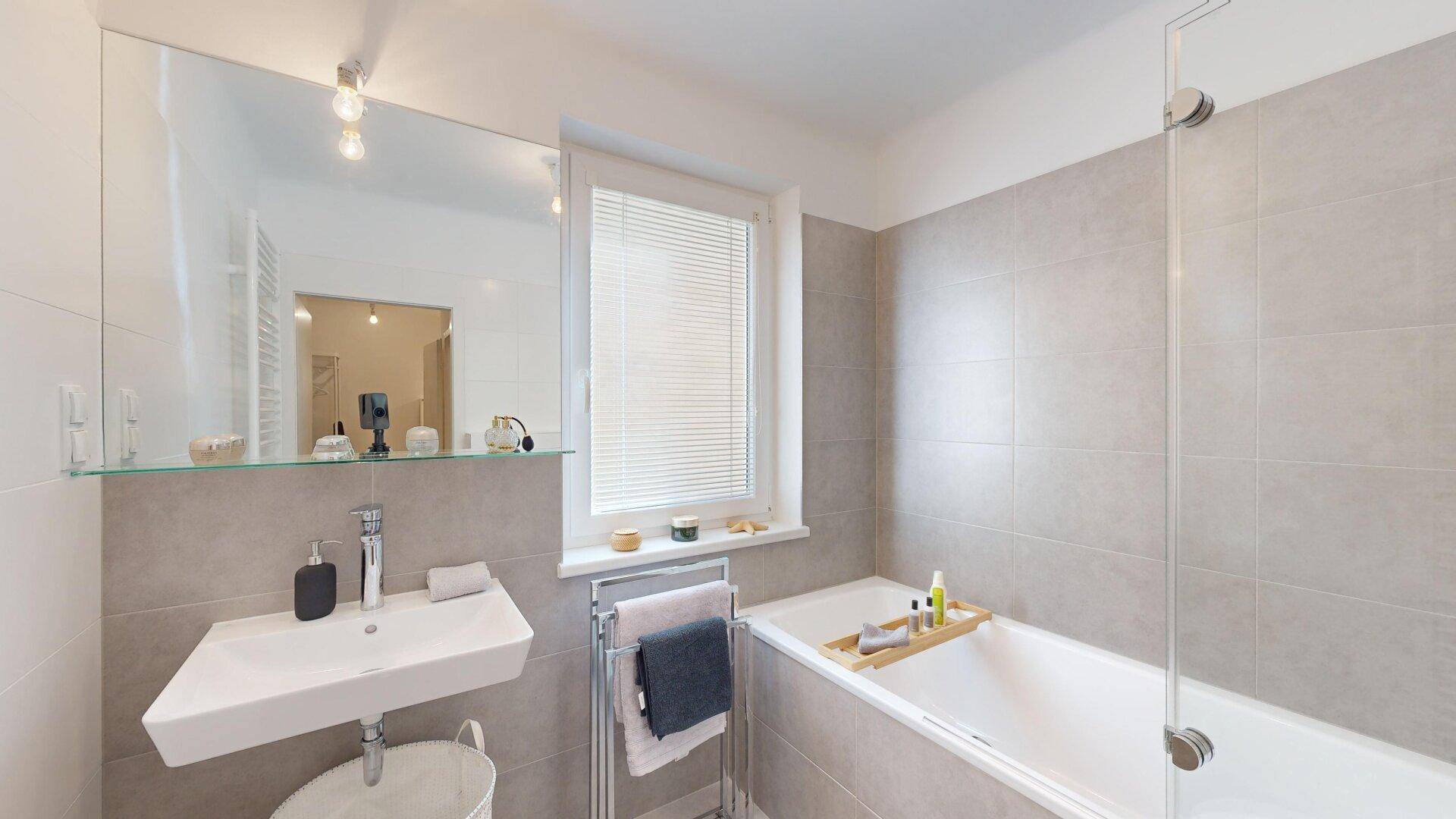 Helles Badezimmer mit Badewanne, modernem Waschbecken und Fenster für natürliche Belüftung.