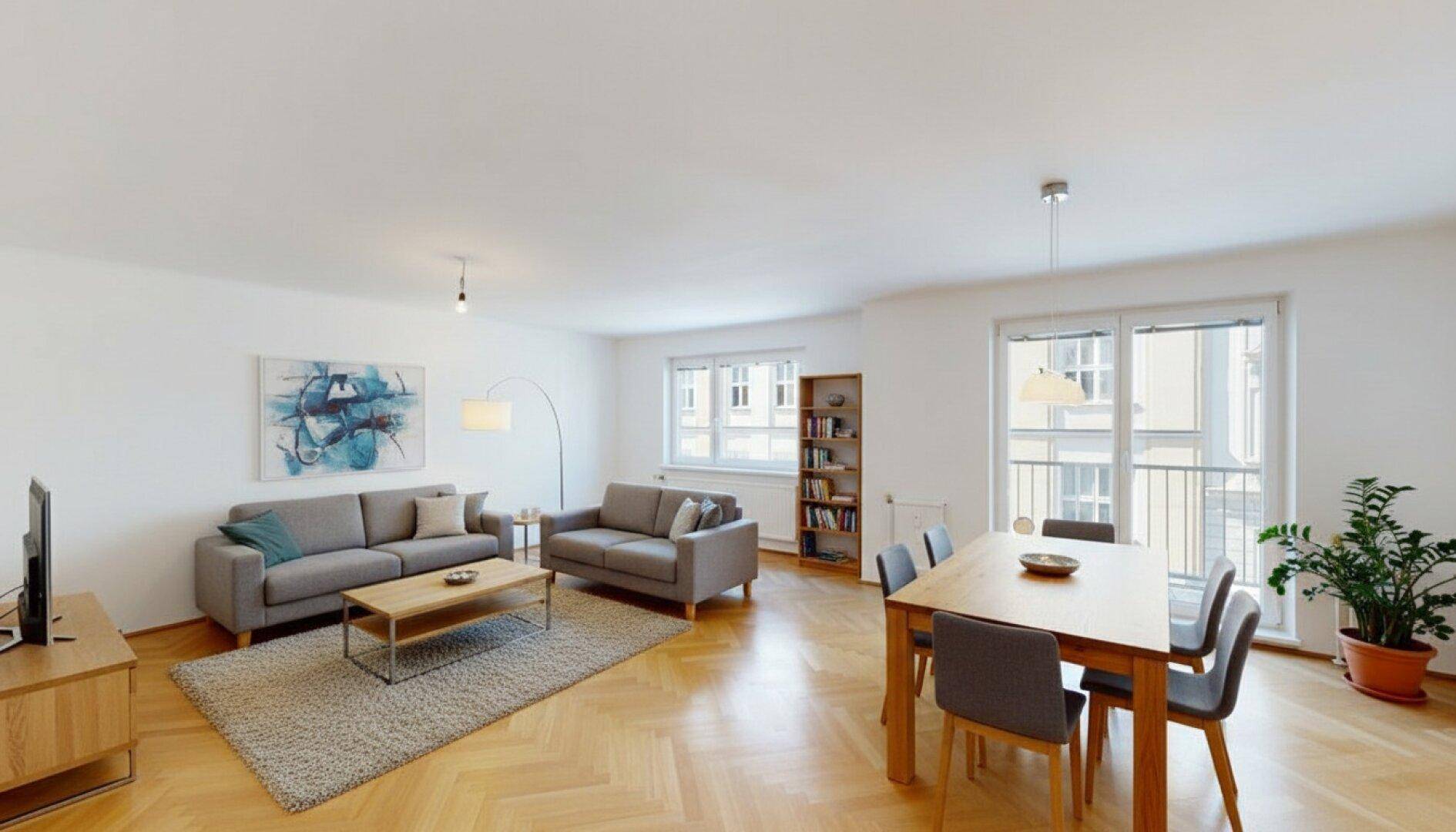 Gemütlicher Wohn- und Essbereich mit Parkettboden, bequemen Sofas und Zugang zum Balkon.