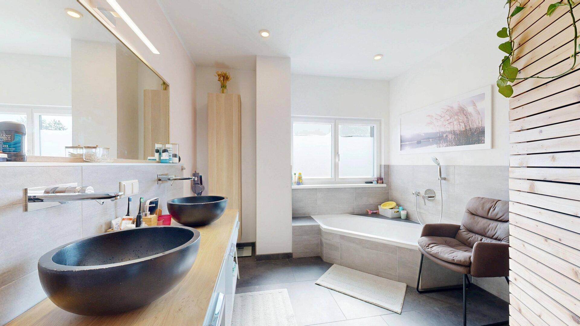 Modernes Badezimmer mit zwei dunklen Aufsatzwaschbecken, Badewanne und Holzdetails.