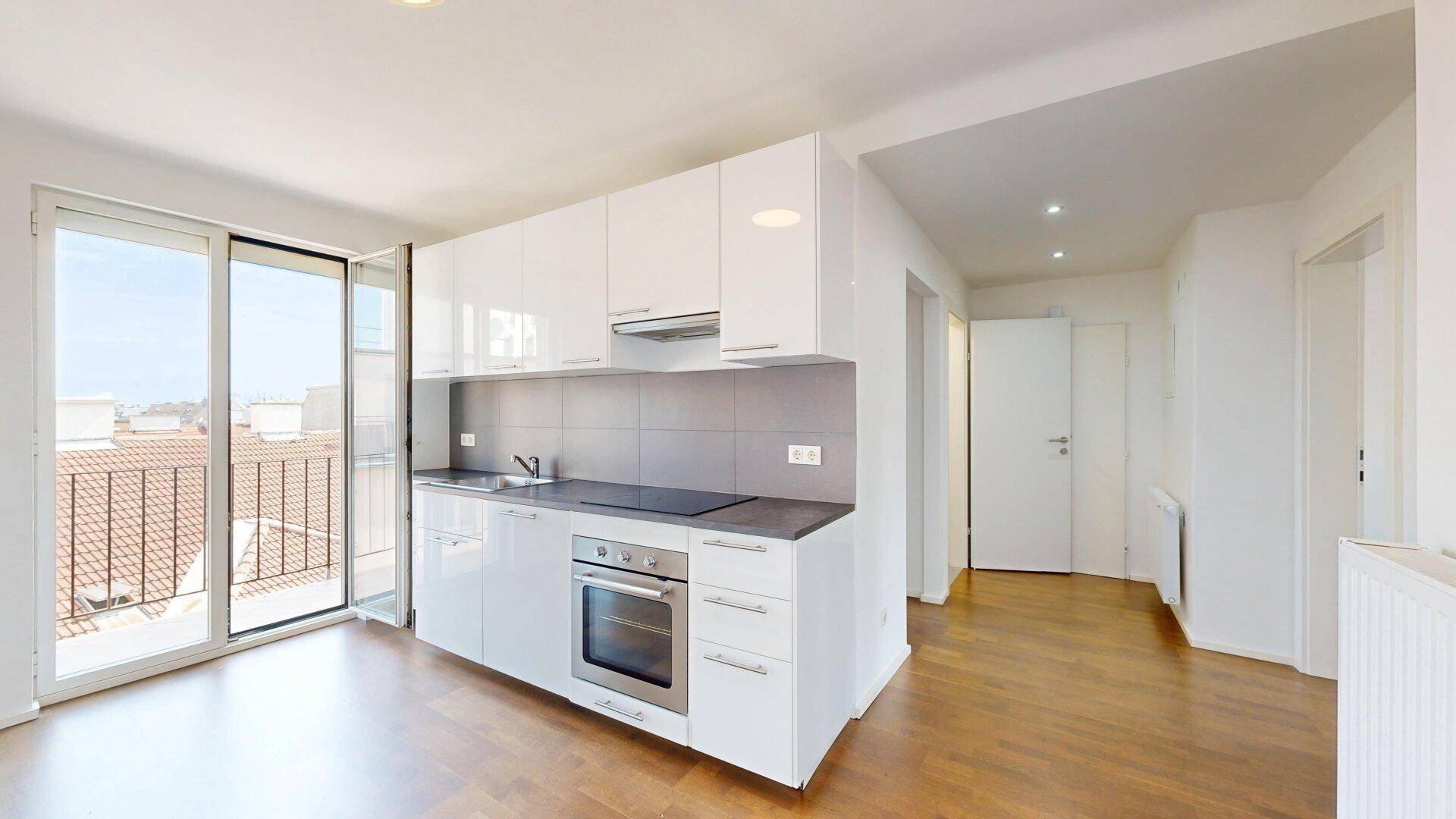 Moderne weiße Einbauküche mit glänzenden Fronten und Zugang zu einem Balkon oder einer Terrasse.