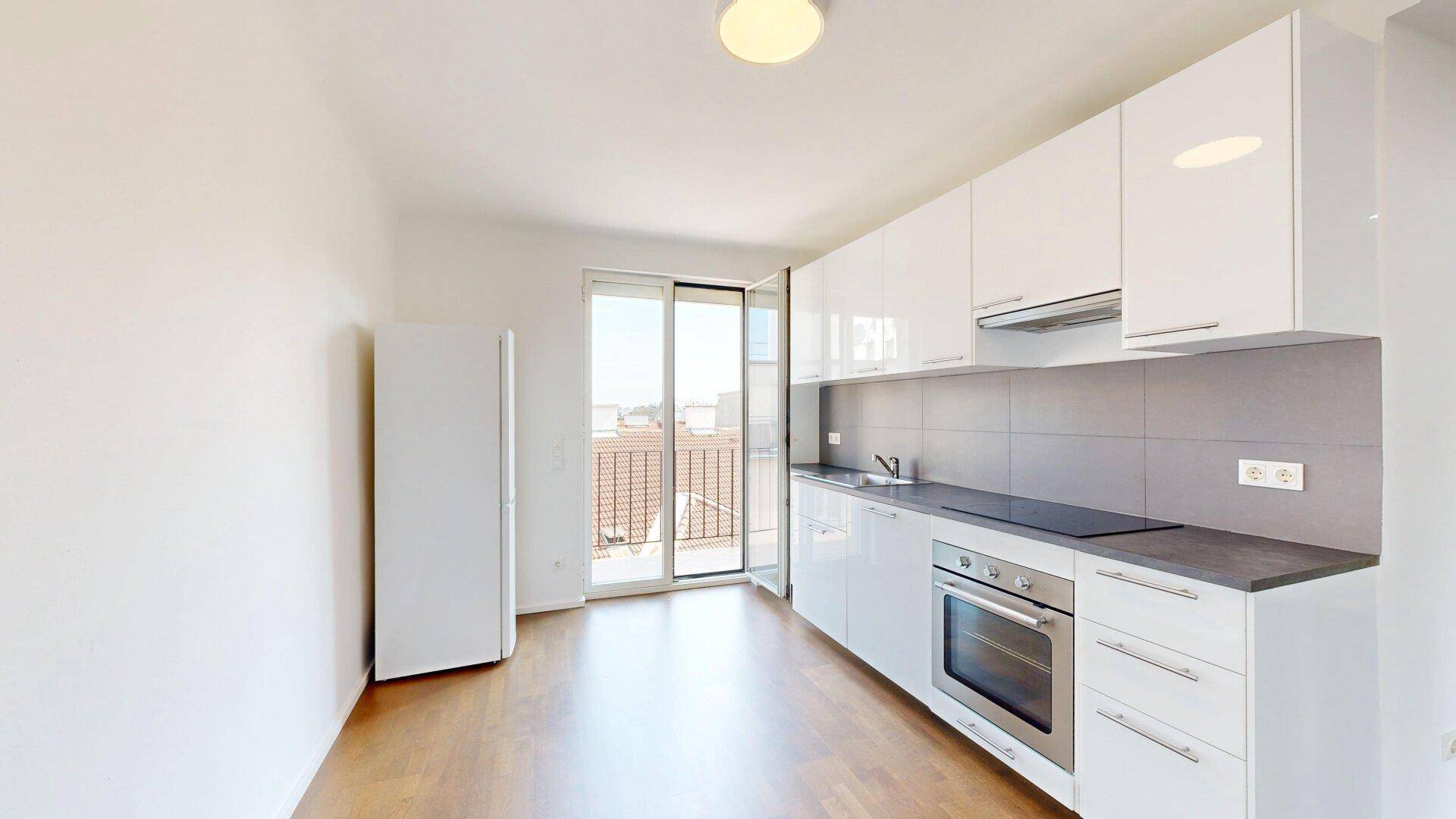 Helle Küche mit weißen Schränken, integriertem Kühlschrank und Zugang zu einem Balkon.