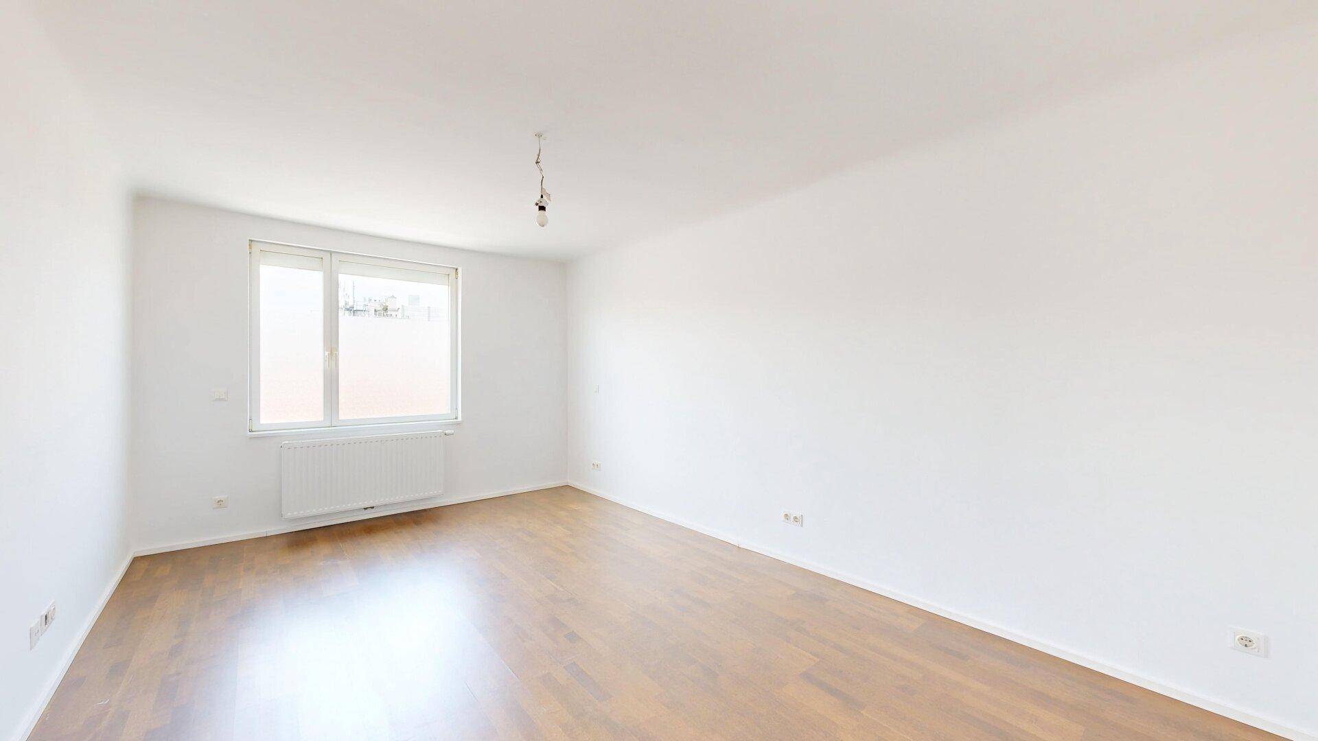 Heller, leerer Raum mit Parkettboden und einem großen Fenster, ideal als Wohnzimmer.