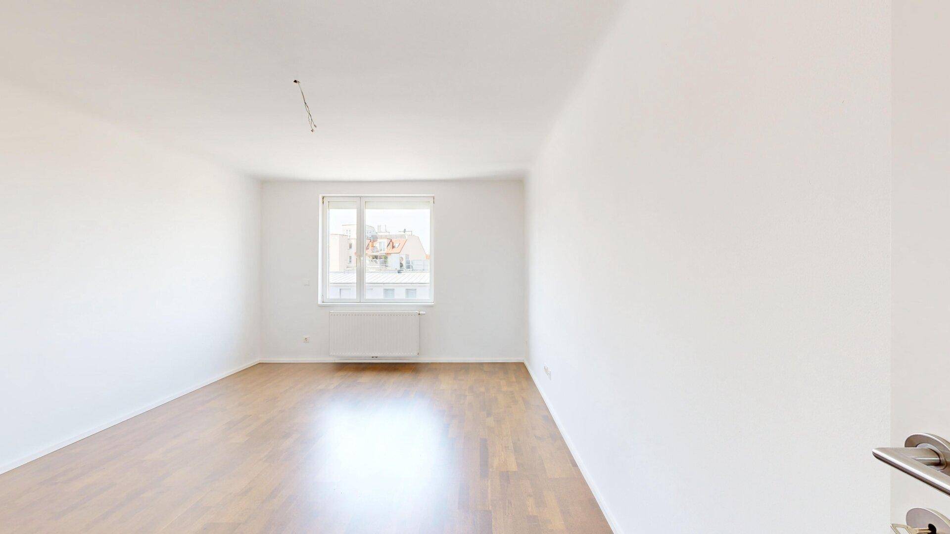 Helles Schlafzimmer mit Parkettboden und einem Fenster, das viel Tageslicht hereinlässt.