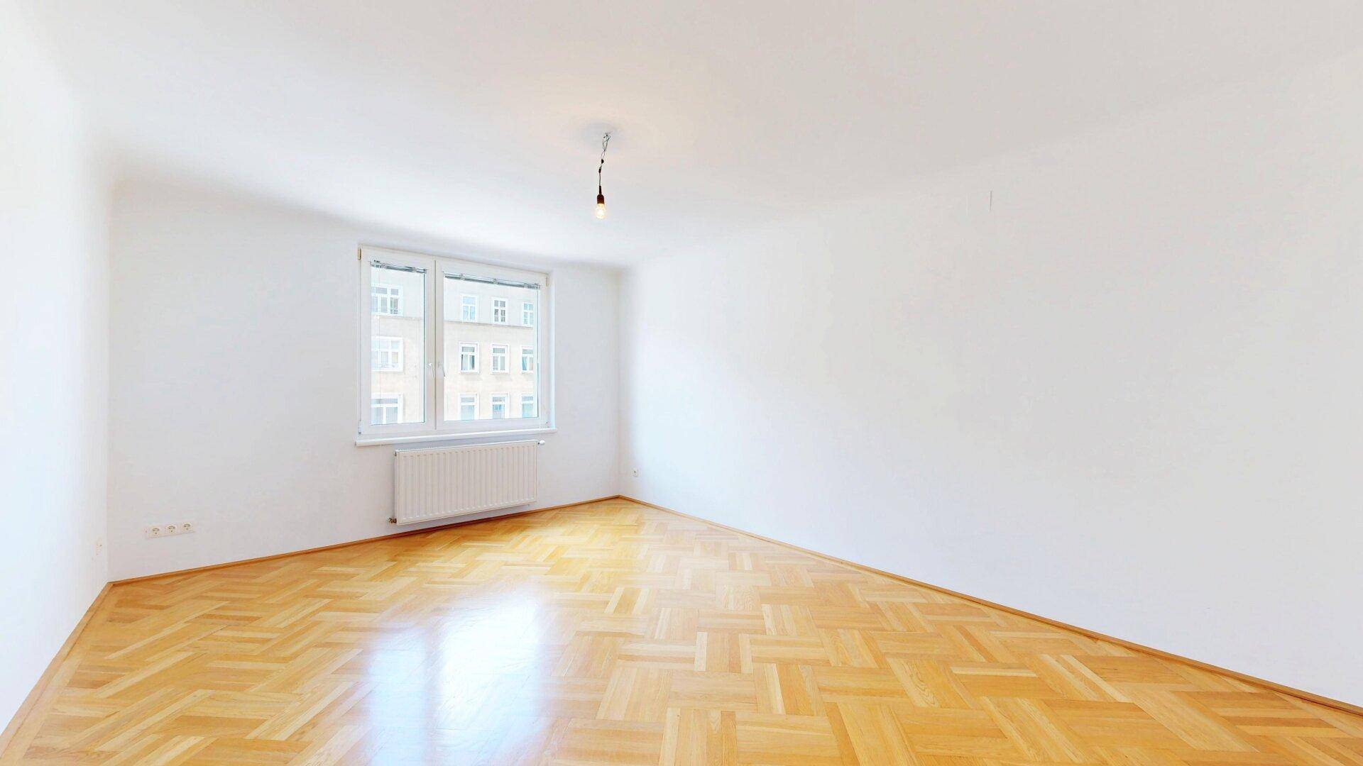 Helles Schlafzimmer mit Fischgrätparkett und einem großen Fenster, das viel Licht spendet.