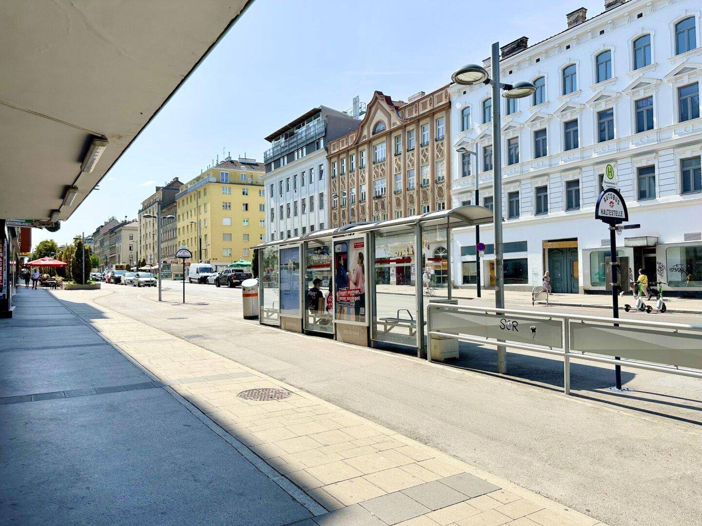 Belebte Straße mit Bushaltestelle, Geschäften und historischen Gebäudefassaden.