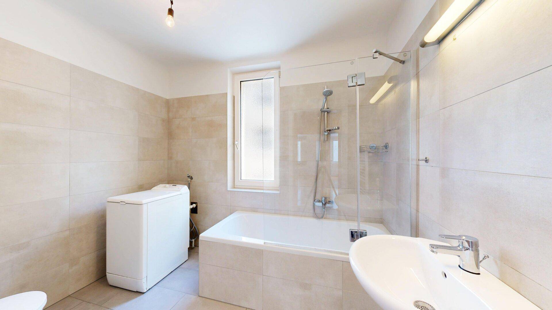 Funktionales Badezimmer mit Badewanne, Dusche und Waschmaschine, hell gefliest.