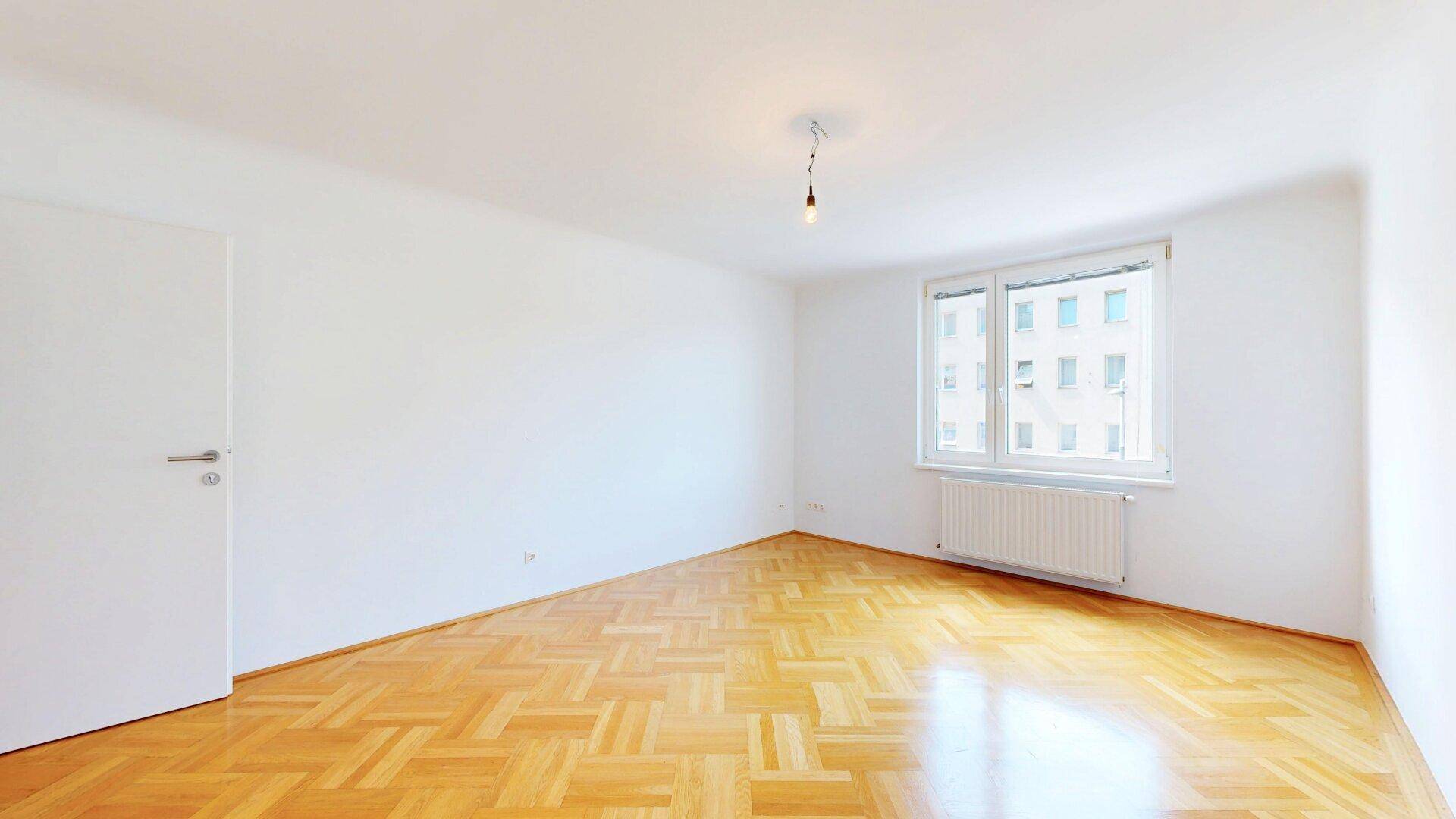 Geräumiges Schlafzimmer mit Fischgrätparkett und einem großen Fenster für viel Tageslicht.