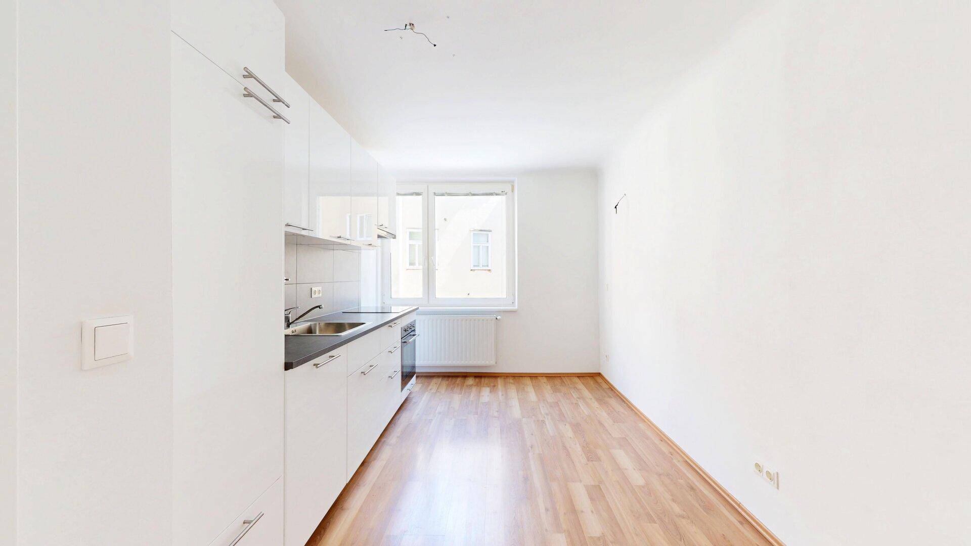 Kleine, helle Küche mit weißen Schränken, Spüle und Kochfeld, ideal für Singles.
