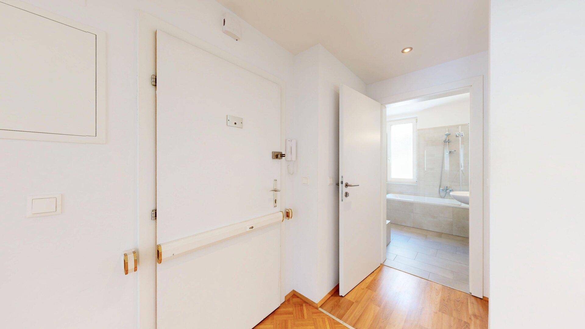 Eingangsbereich mit Holzboden und Zugang zu einem Badezimmer und weiteren Räumen.