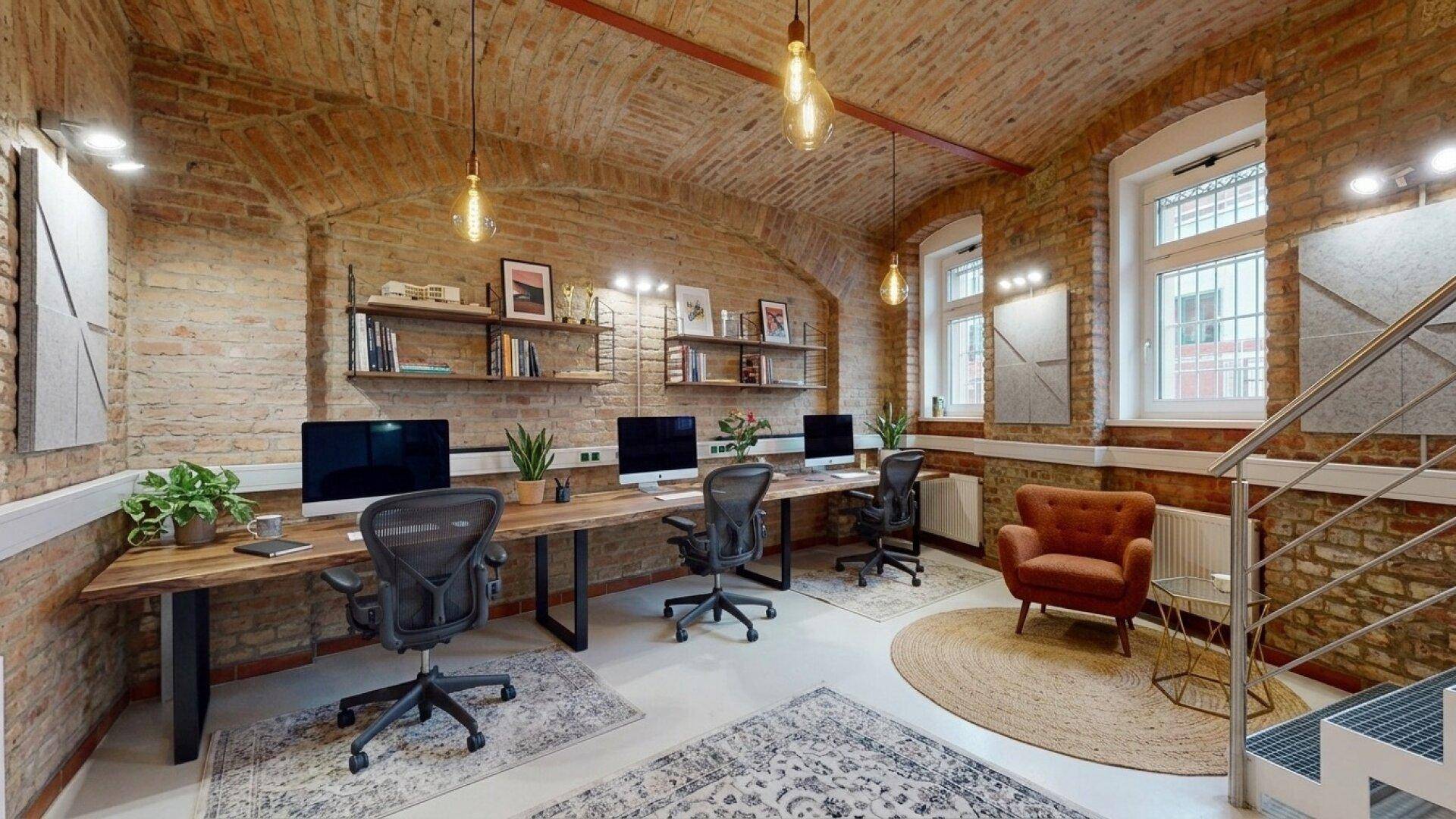 Modern eingerichtetes Büro mit Ziegelwänden, Gewölbedecke und mehreren Arbeitsplätzen.