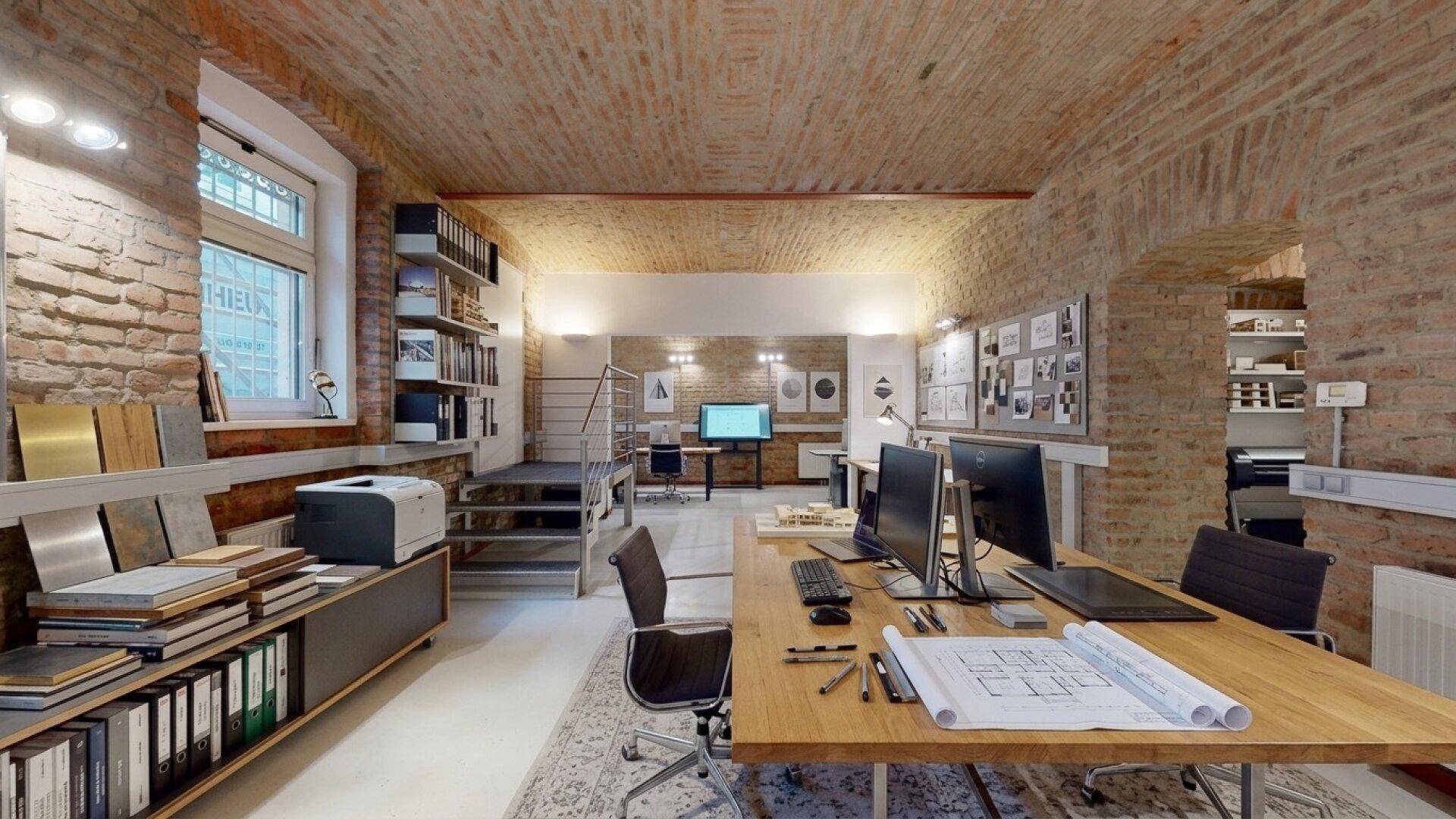 Modernes Architekturbüro mit Ziegelwänden, Gewölbedecke und mehreren Arbeitsplätzen.