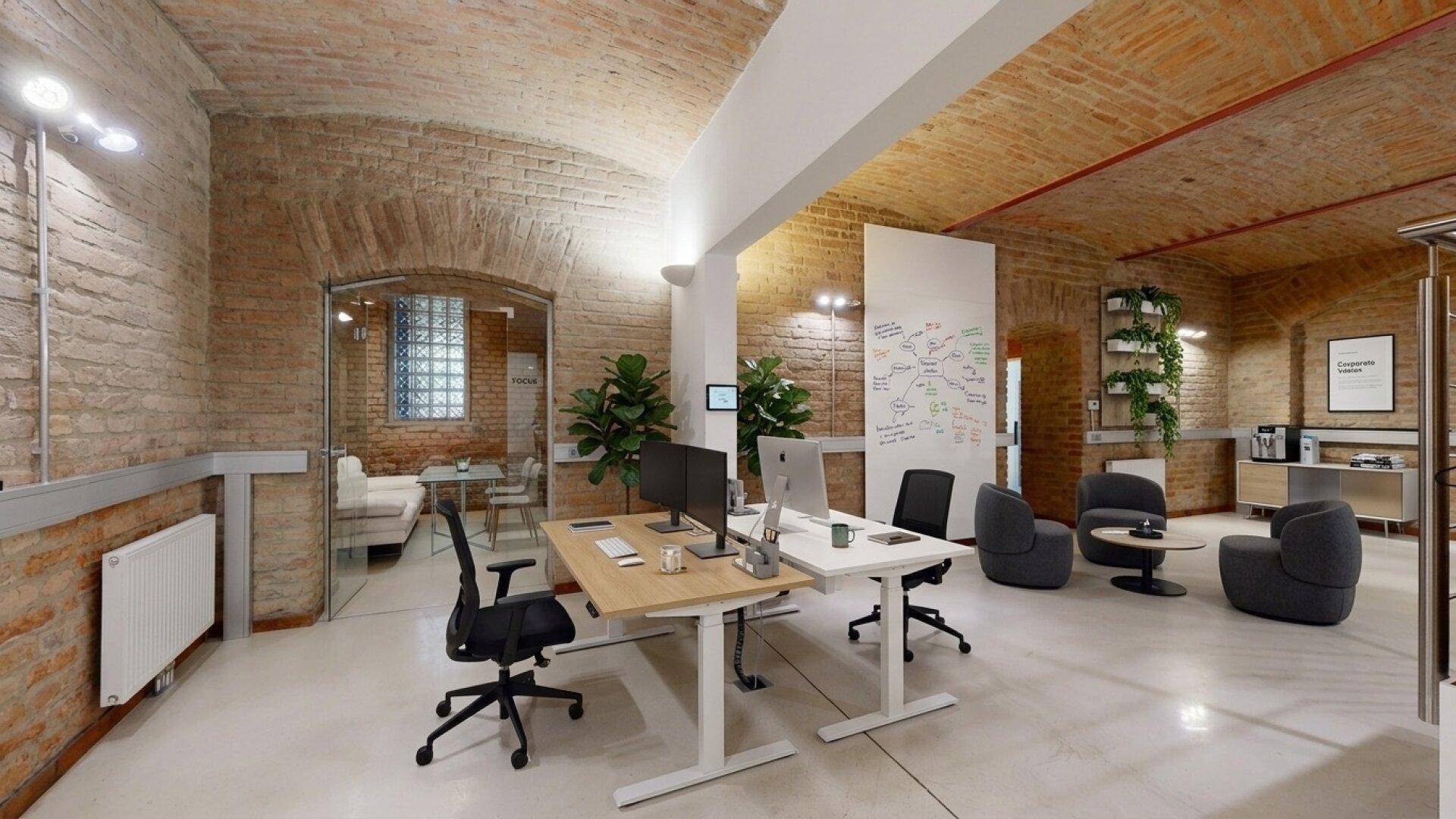 Modernes Büro mit Ziegelwänden, Gewölbedecke und einem Besprechungsbereich hinter Glas.