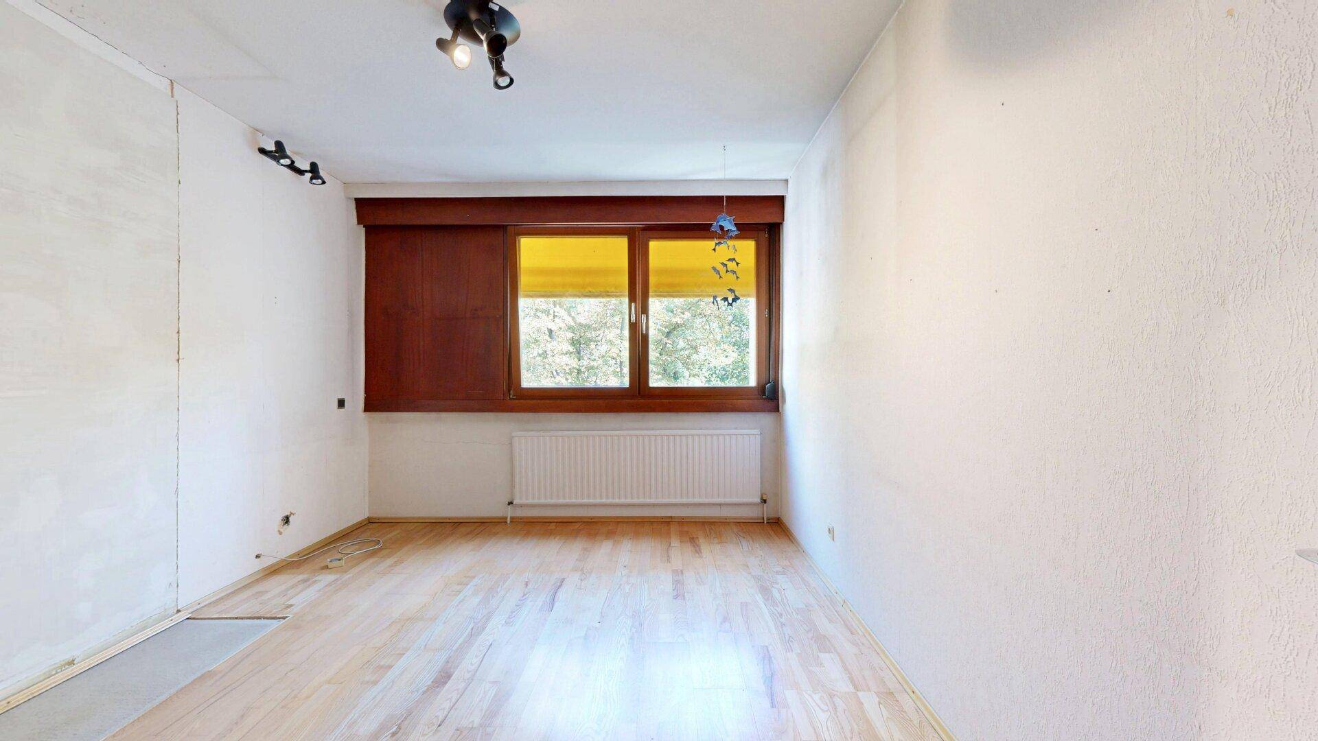 Geräumiges Schlafzimmer mit hellem Parkettboden und Fenster mit gelben Jalousien.