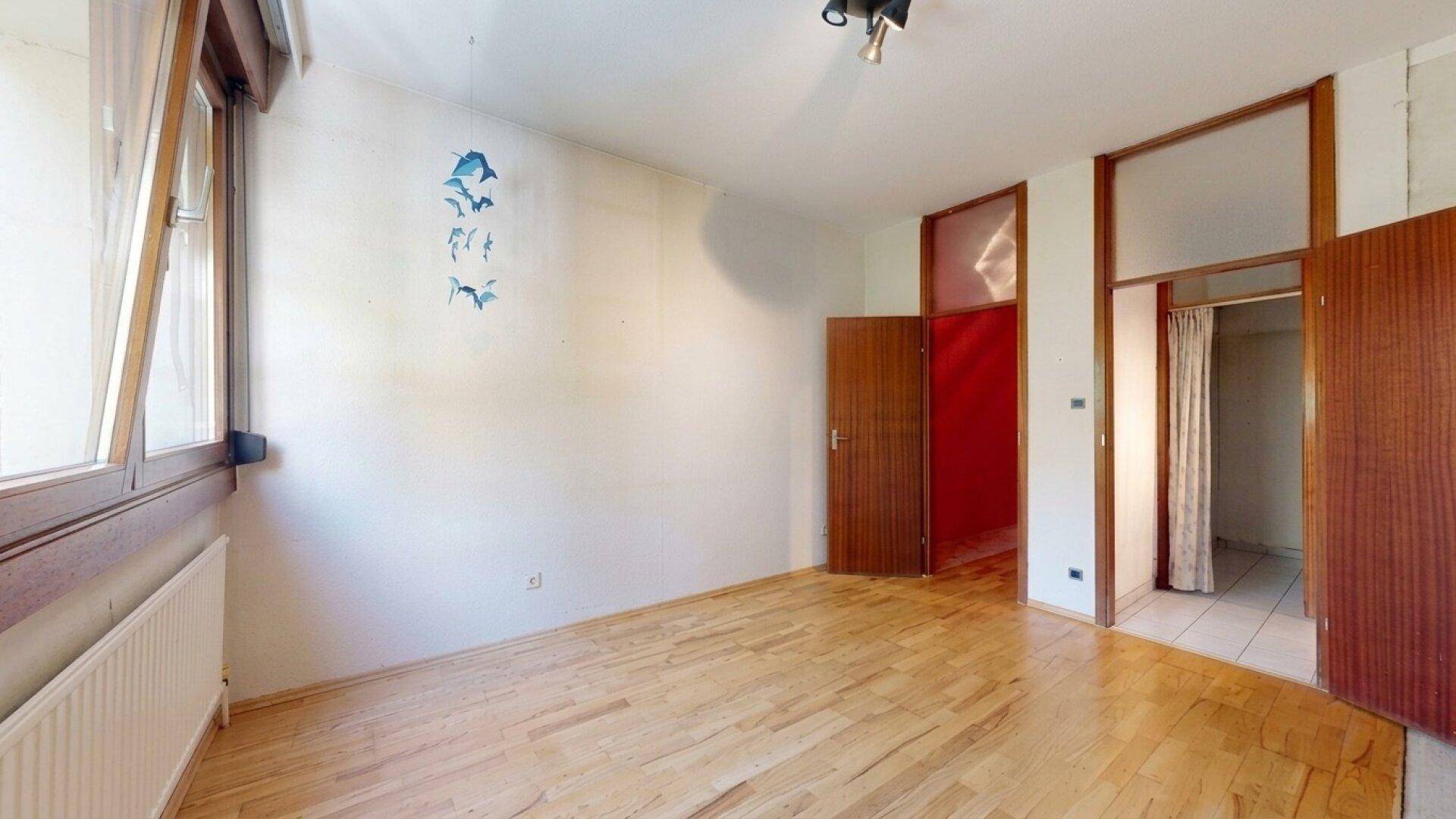 Helles Schlafzimmer mit Parkettboden und Fenster, bereit zur individuellen Gestaltung.