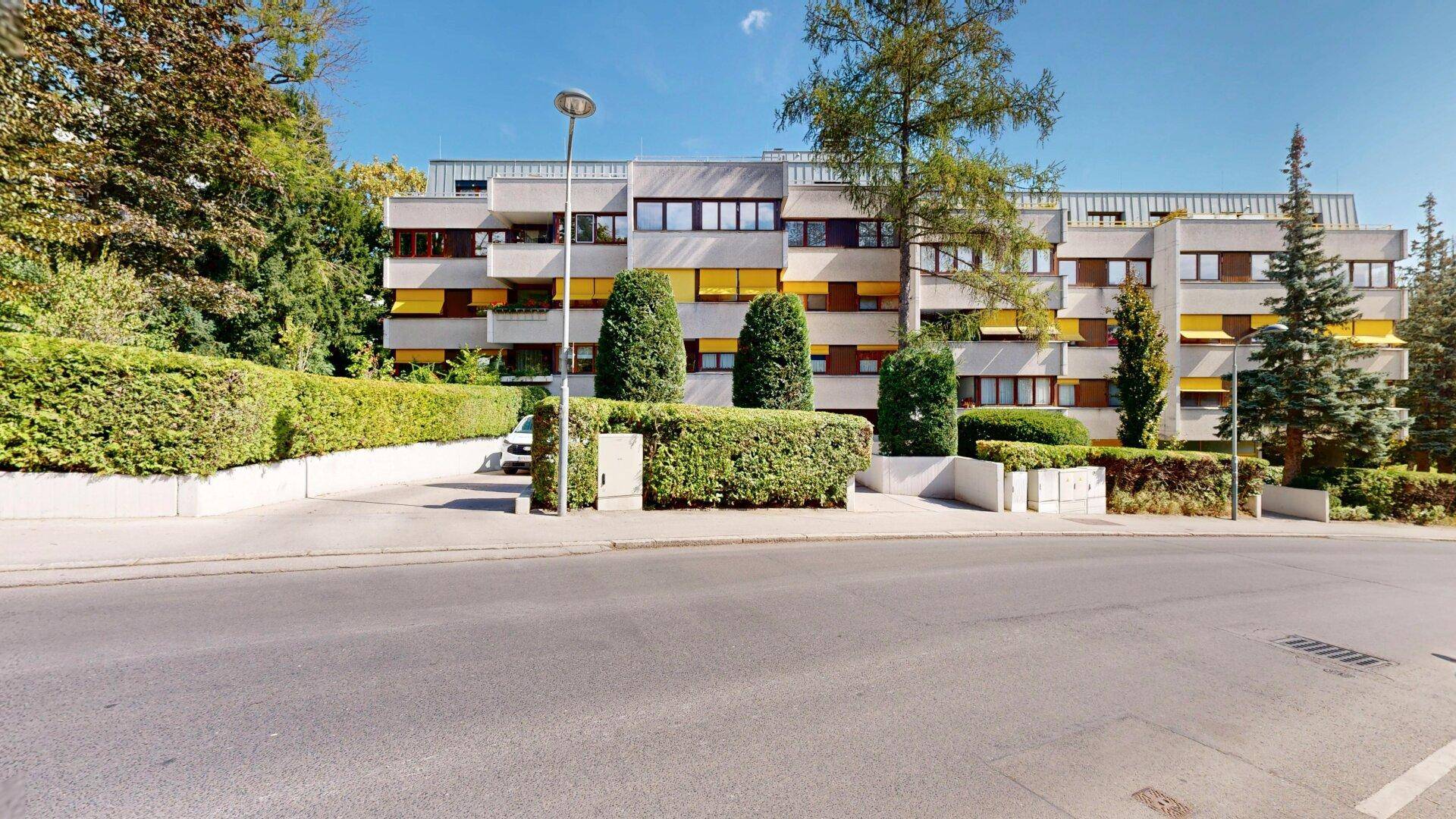 Mehrfamilienhaus mit gelben Markisen an den Balkonen und gepflegter Außenanlage.