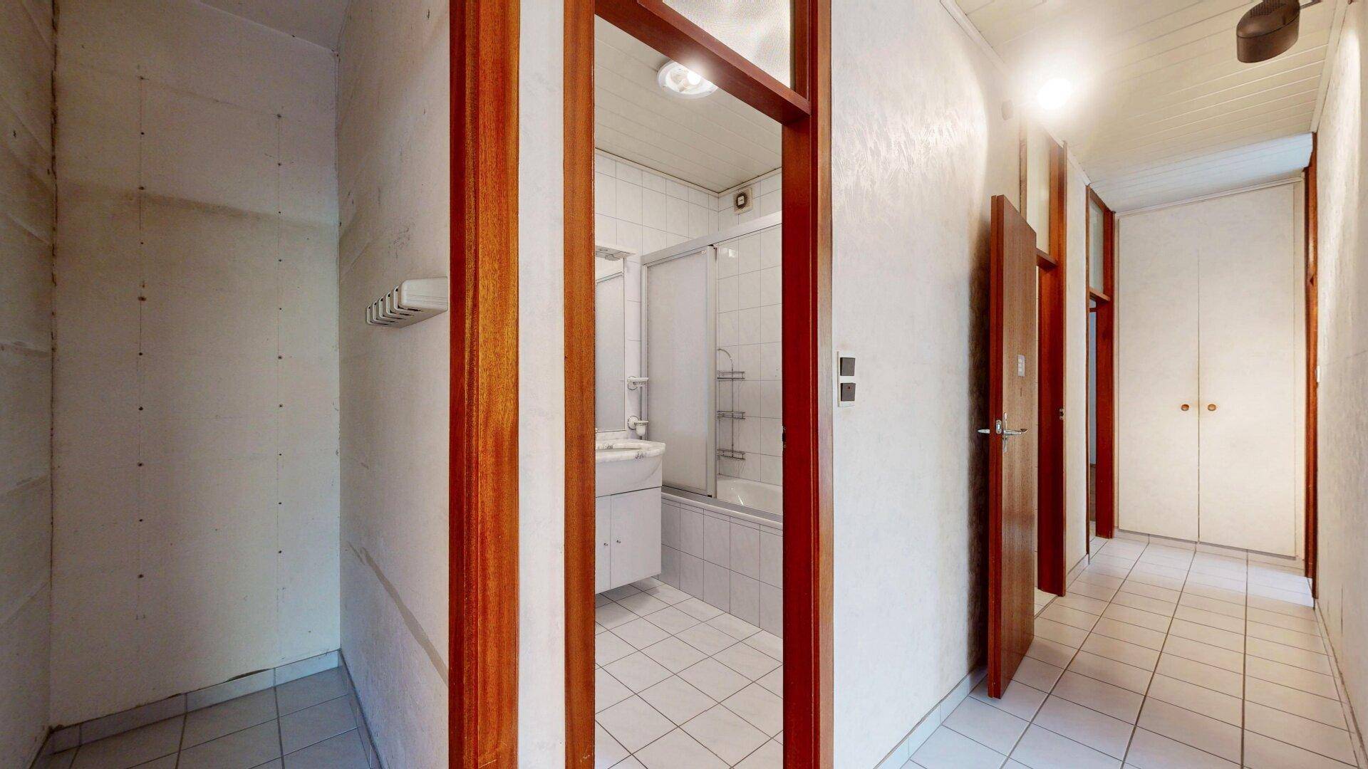 Flur mit Fliesenboden und Zugang zu einem Badezimmer mit Badewanne und Dusche.