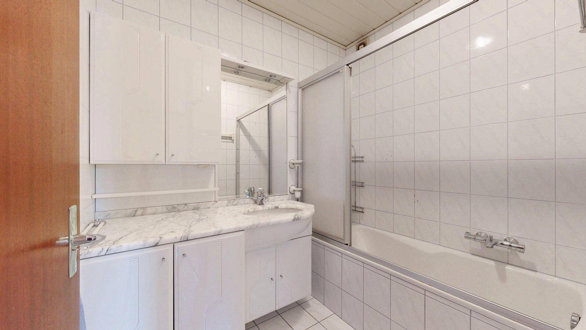 Badezimmer mit Badewanne, Duschwand, Marmorwaschtisch und weißen Fliesen.