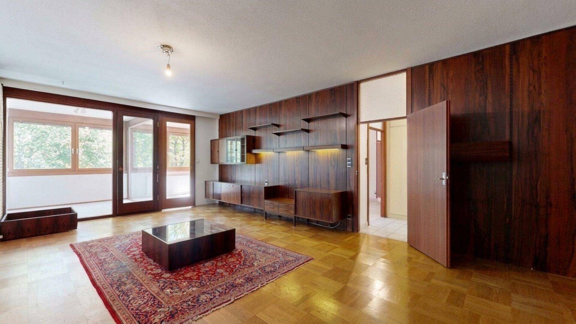 Wohnzimmer mit Holzwandverkleidung, integrierten Regalen und Zugang zu einem sonnigen Außenbereich.