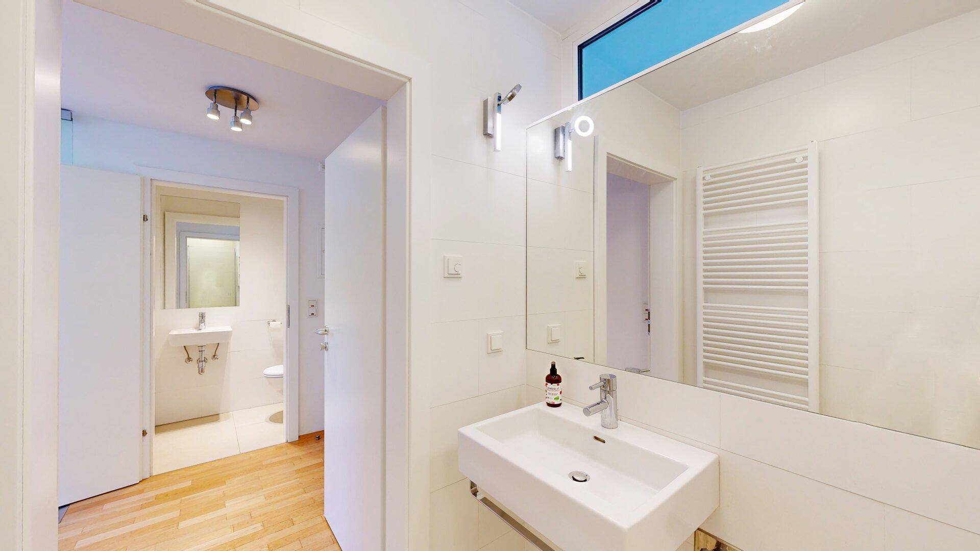 Helles Badezimmer mit modernem Waschbecken, großem Spiegel und Zugang zu einem separaten WC.