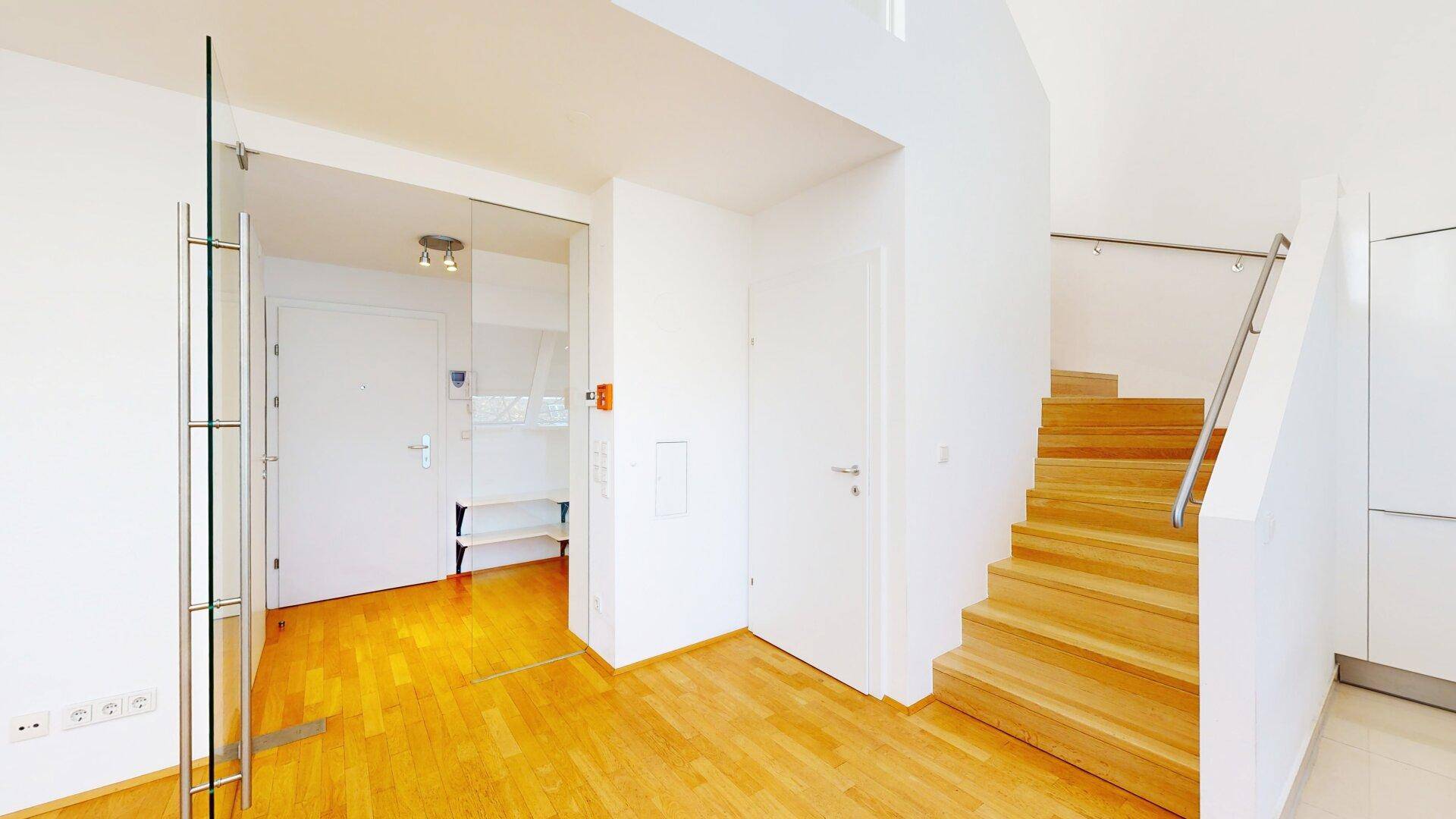 Heller Eingangsbereich mit Holzboden, Treppe zum Obergeschoss und Glastür.