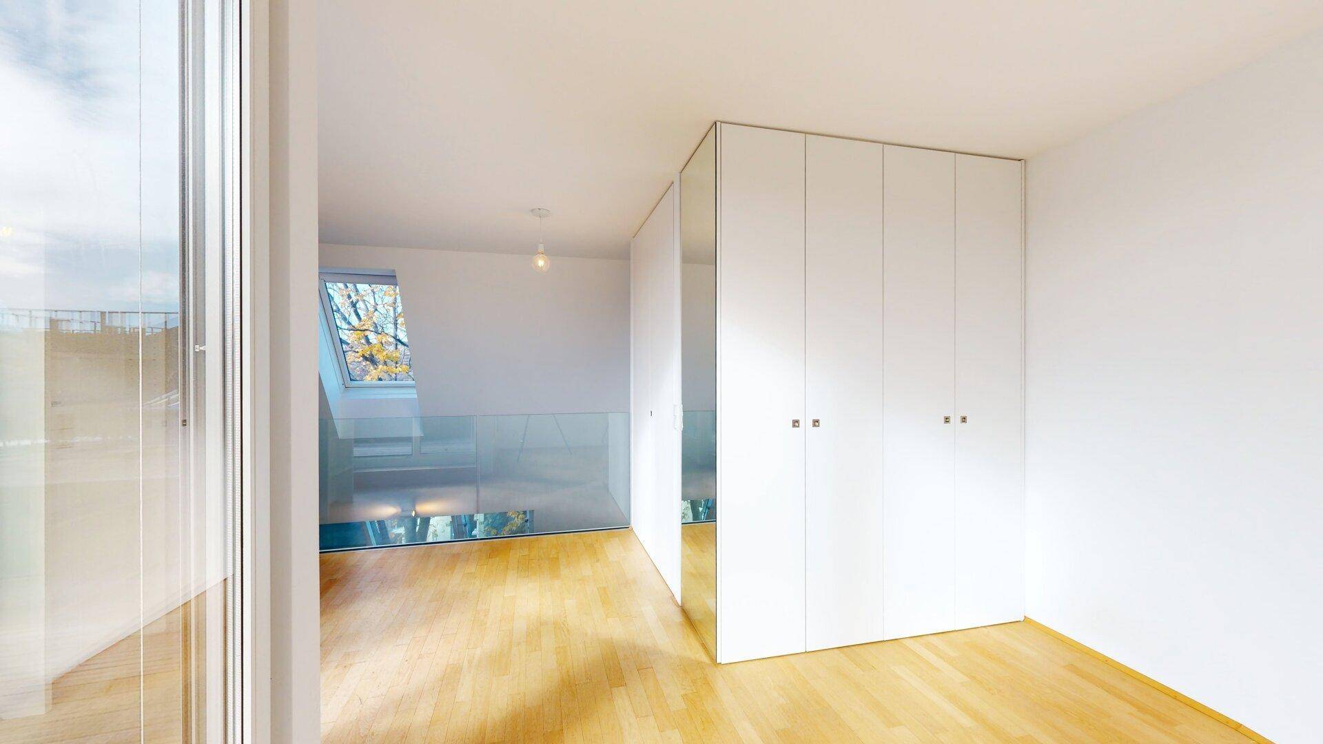 Heller Flur mit Holzboden, Einbauschränken und Blick auf die Dachterrasse durch ein Fenster.