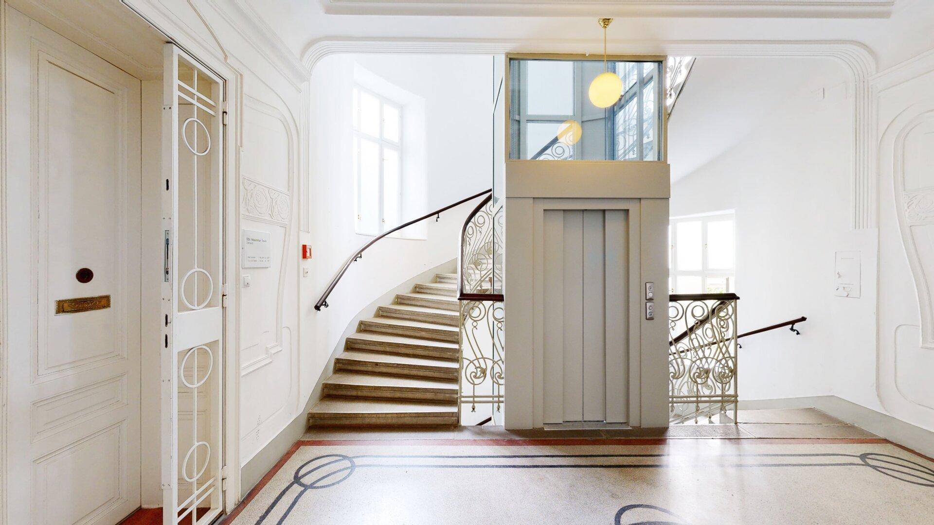 Elegantes Treppenhaus mit historischem Charme, kunstvollem Geländer und modernem Aufzug.