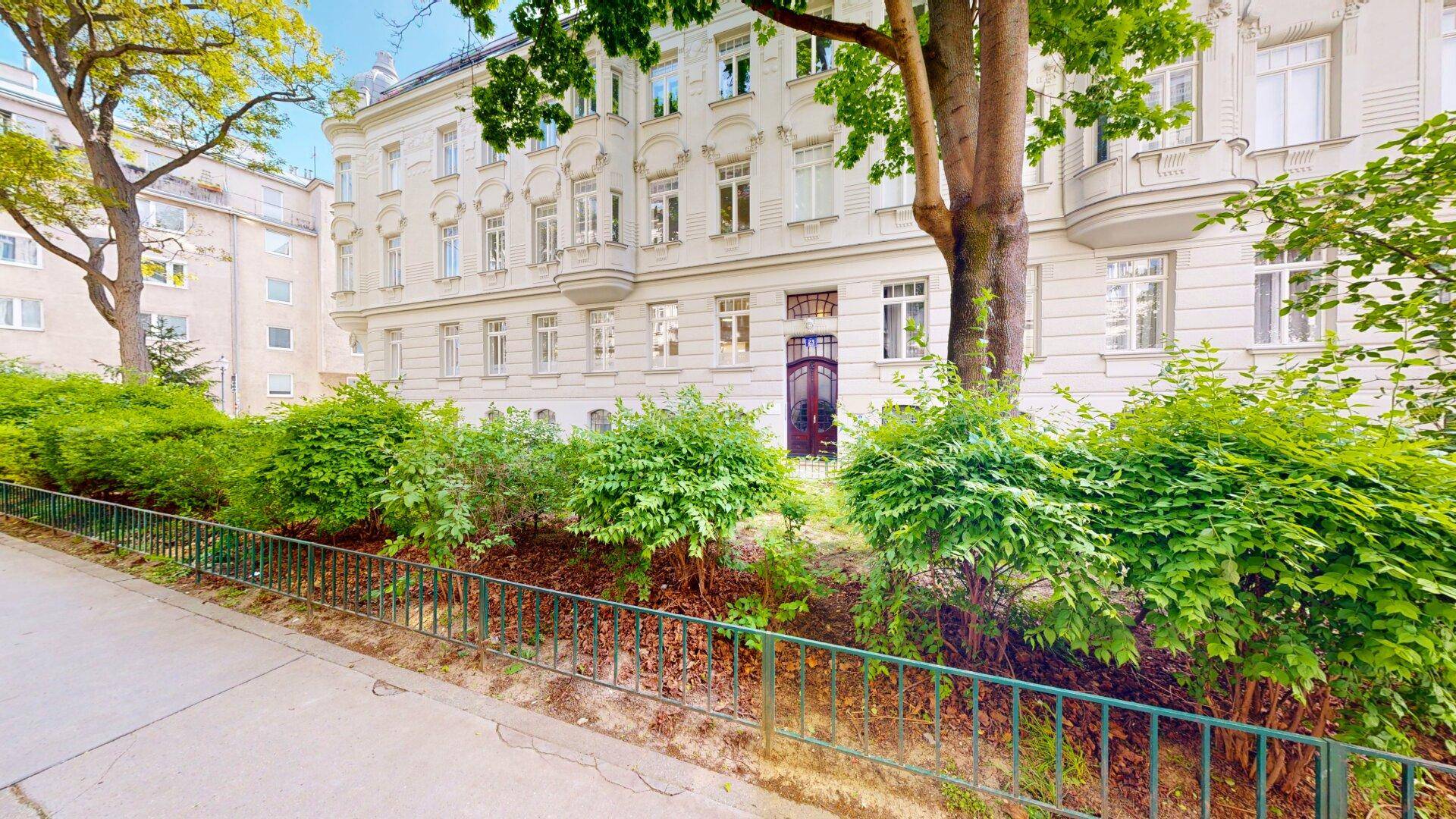 Klassische Fassade eines Altbaus mit vielen Fenstern und grüner Bepflanzung im Vordergrund.