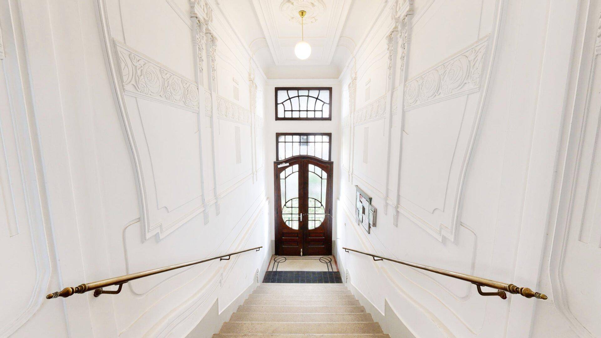 Historisches Treppenhaus mit Stuckverzierungen, eleganten Handläufen und hohen Decken.
