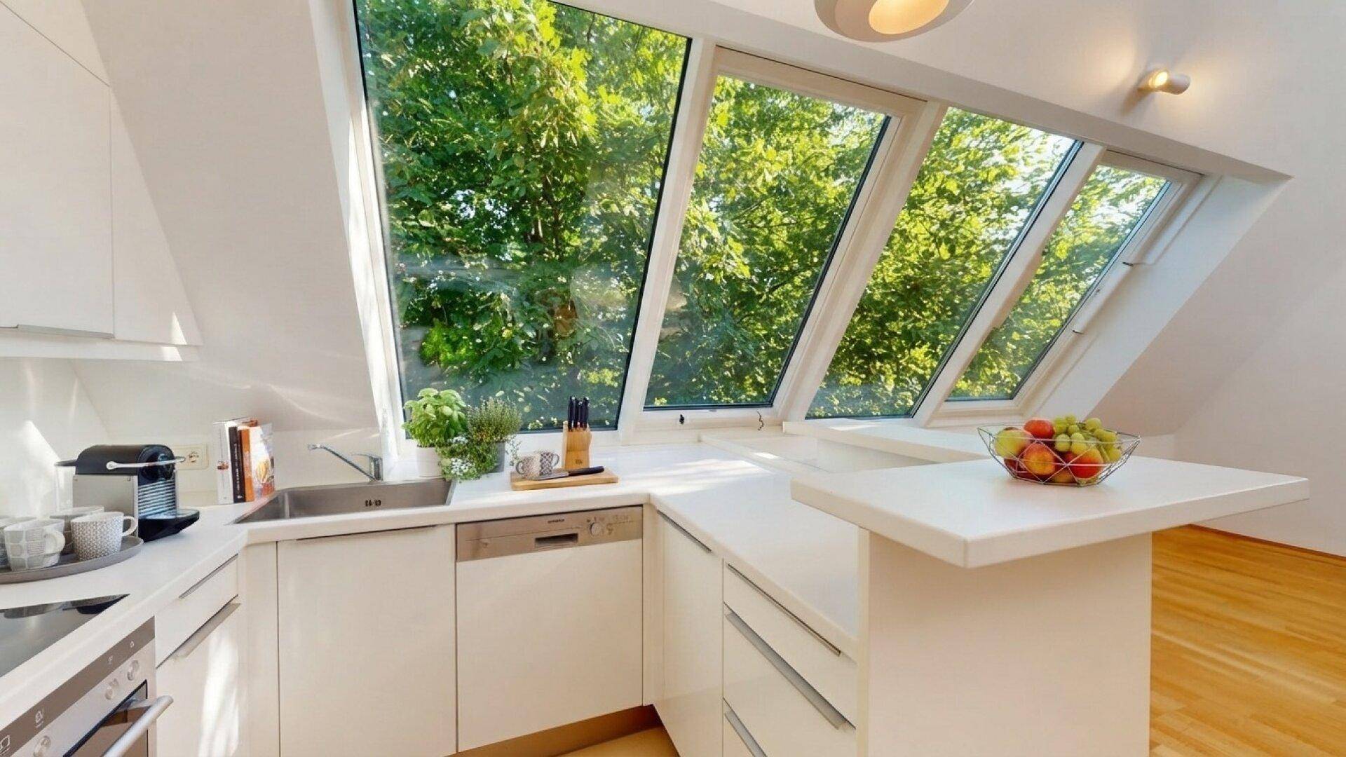 Moderne Einbauküche mit weißen Fronten, Spülmaschine und viel Tageslicht durch große Dachfenster.