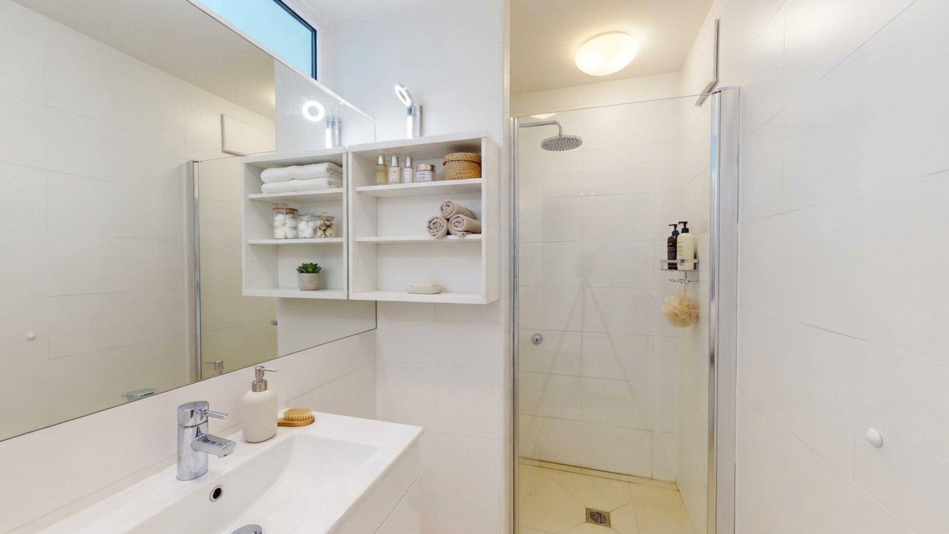 Modernes Badezimmer mit begehbarer Dusche, großem Spiegel und integrierten Ablagen.