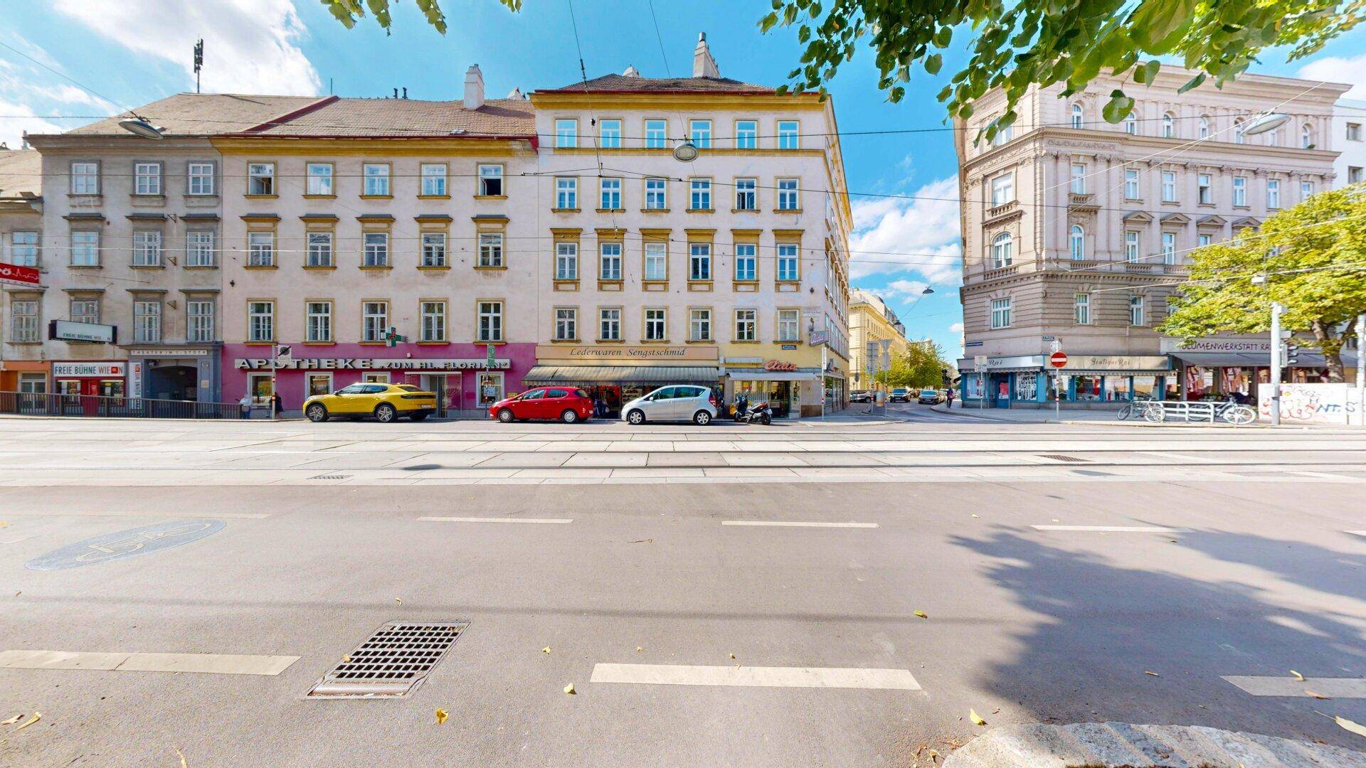 Belebtes Stadtbild mit historischen Gebäuden, parkenden Autos und Straßenbahnschienen.