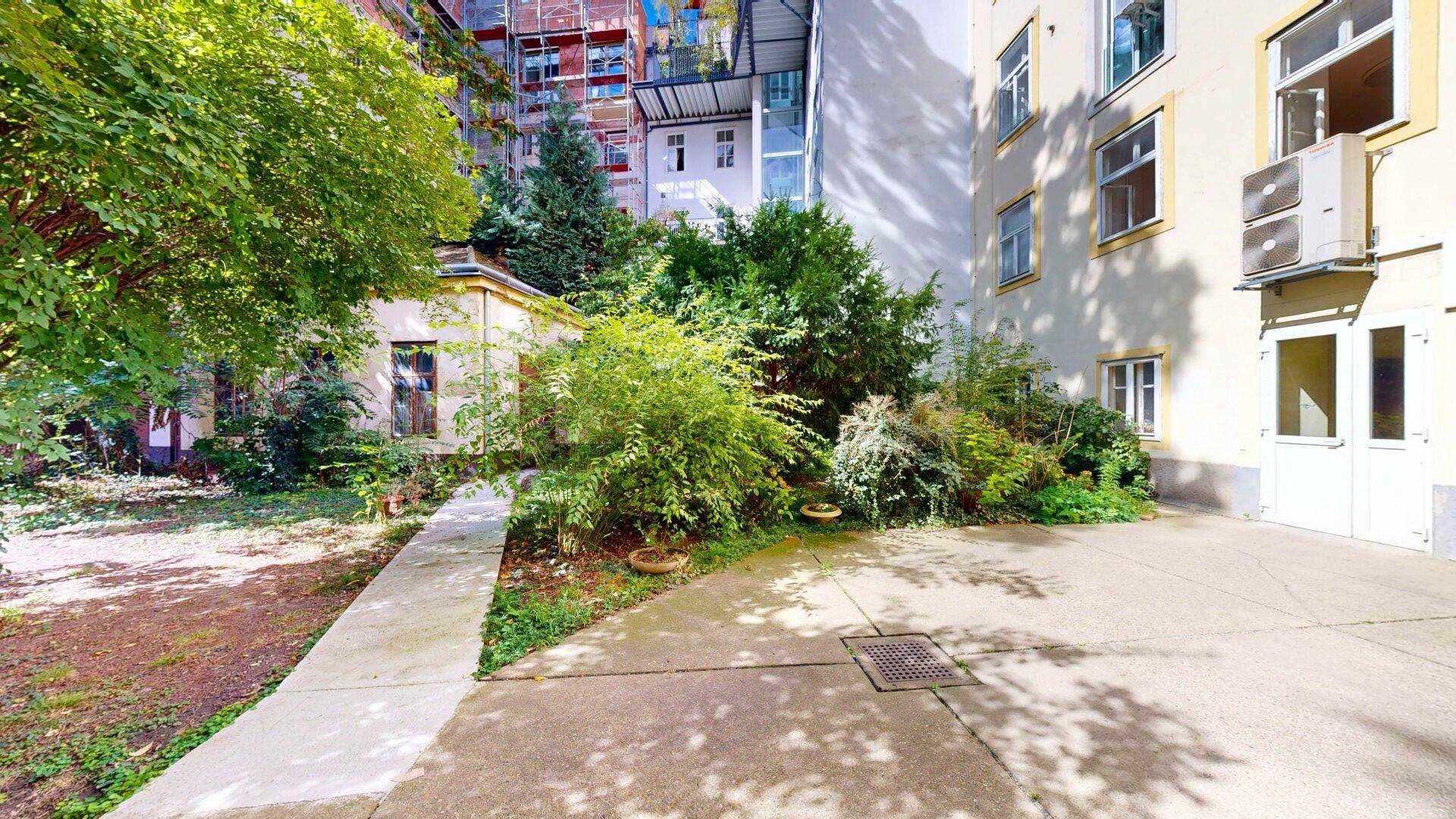 Grüner Innenhofgarten mit üppiger Vegetation, Bäumen und einem kleinen Nebengebäude.