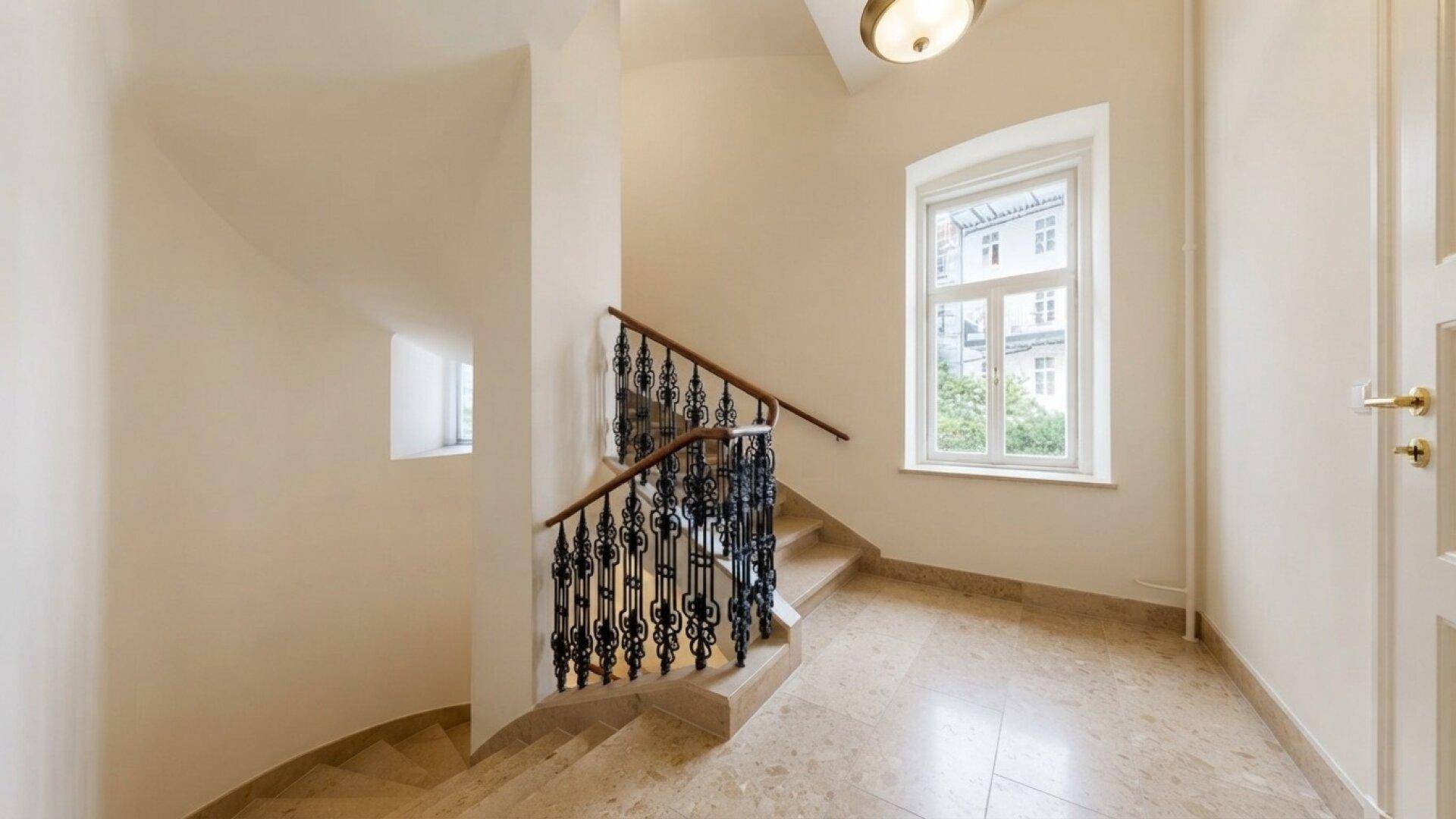 Elegantes Treppenhaus mit Marmorboden, schmiedeeisernem Geländer und großem Fenster.