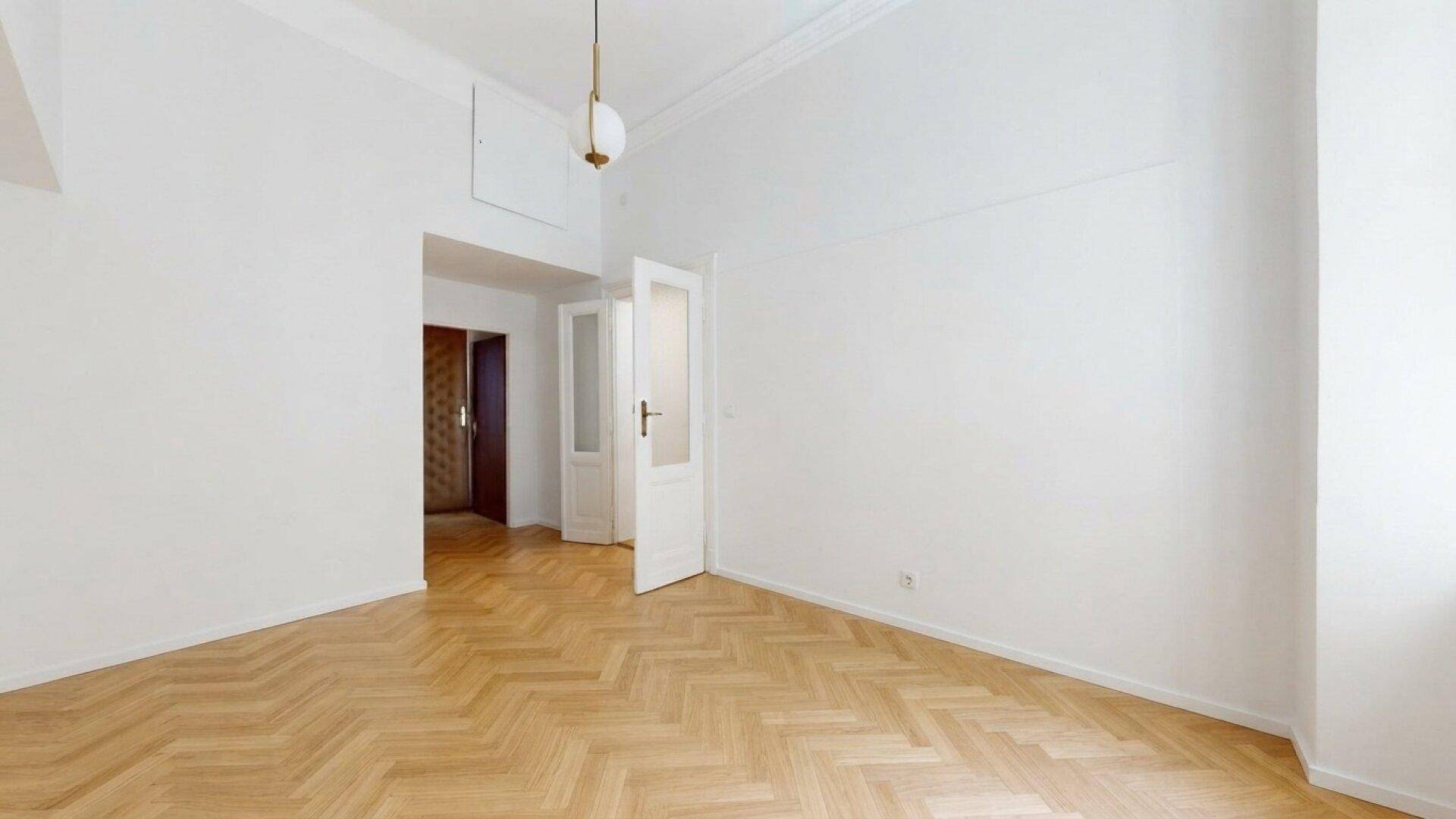 Leerer Raum mit Fischgrätparkett, weißen Wänden und einer Tür mit Glaseinsätzen.