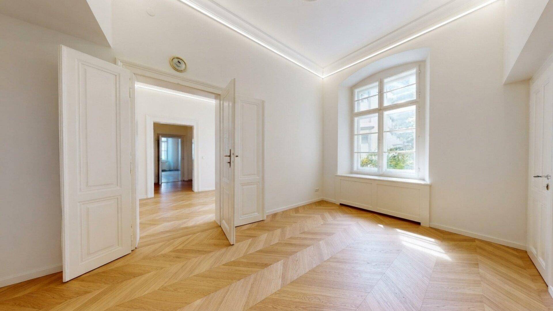 Geräumiger Raum mit Fischgrätparkett, hohen Decken und einem großen Bogenfenster.