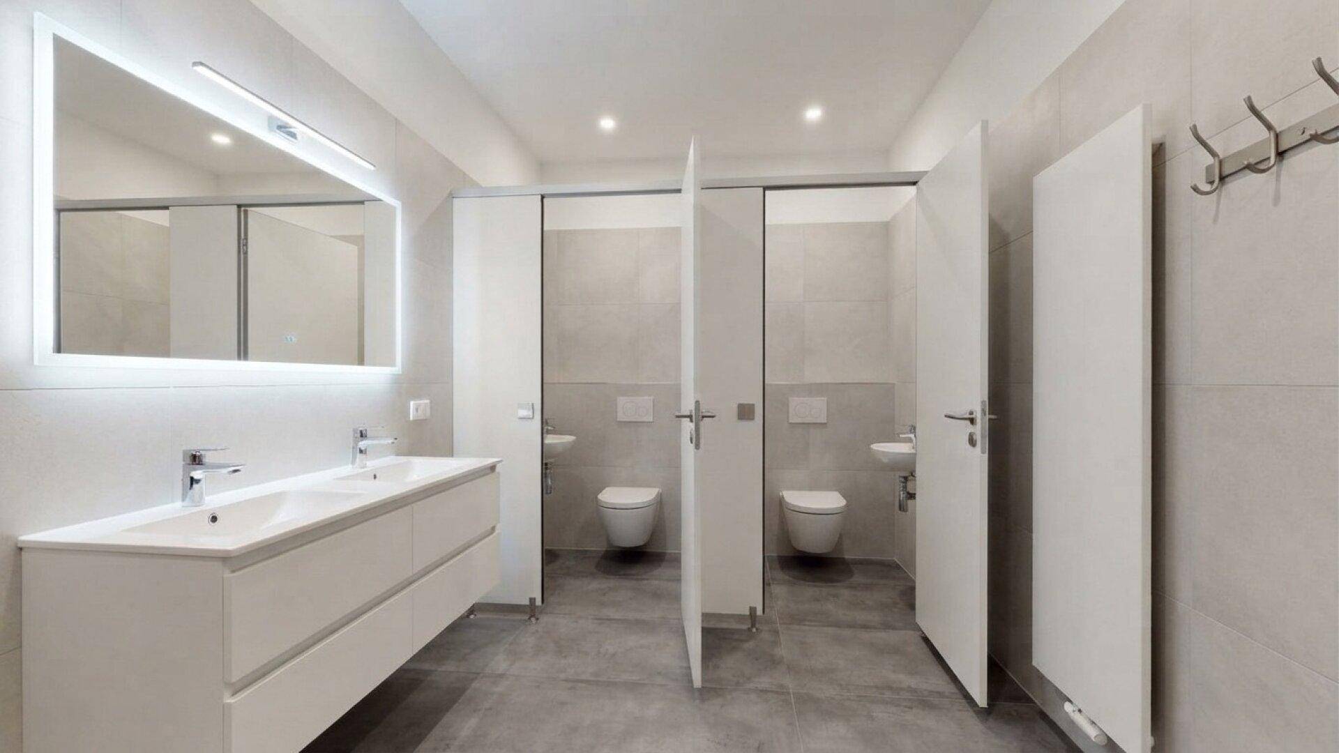 Moderner öffentlicher Waschraum mit mehreren Toilettenkabinen und einem Doppelwaschtisch.