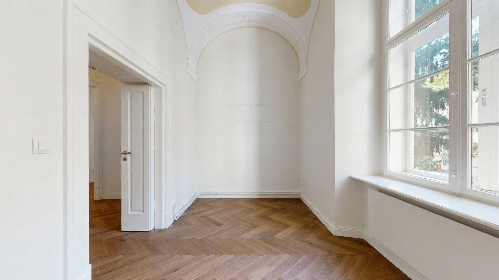 Eleganter Raum mit Fischgrätparkett, hohen Fenstern und dekorativer Deckenverzierung.