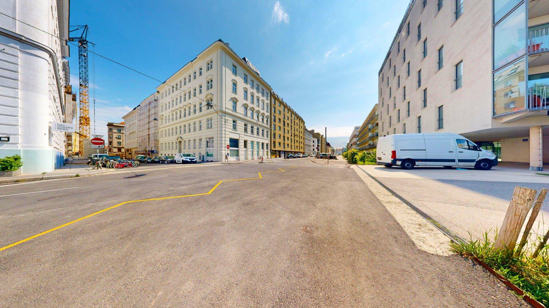 Weitläufige Straßenansicht mit historischen Gebäuden und modernen Bauten unter blauem Himmel.
