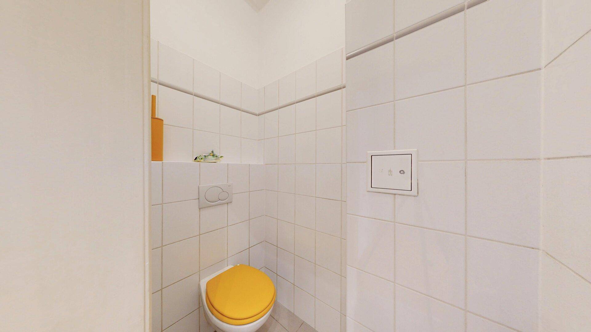 Separate Toilette mit weißen Fliesen, gelbem Toilettensitz und einfacher Ausstattung.