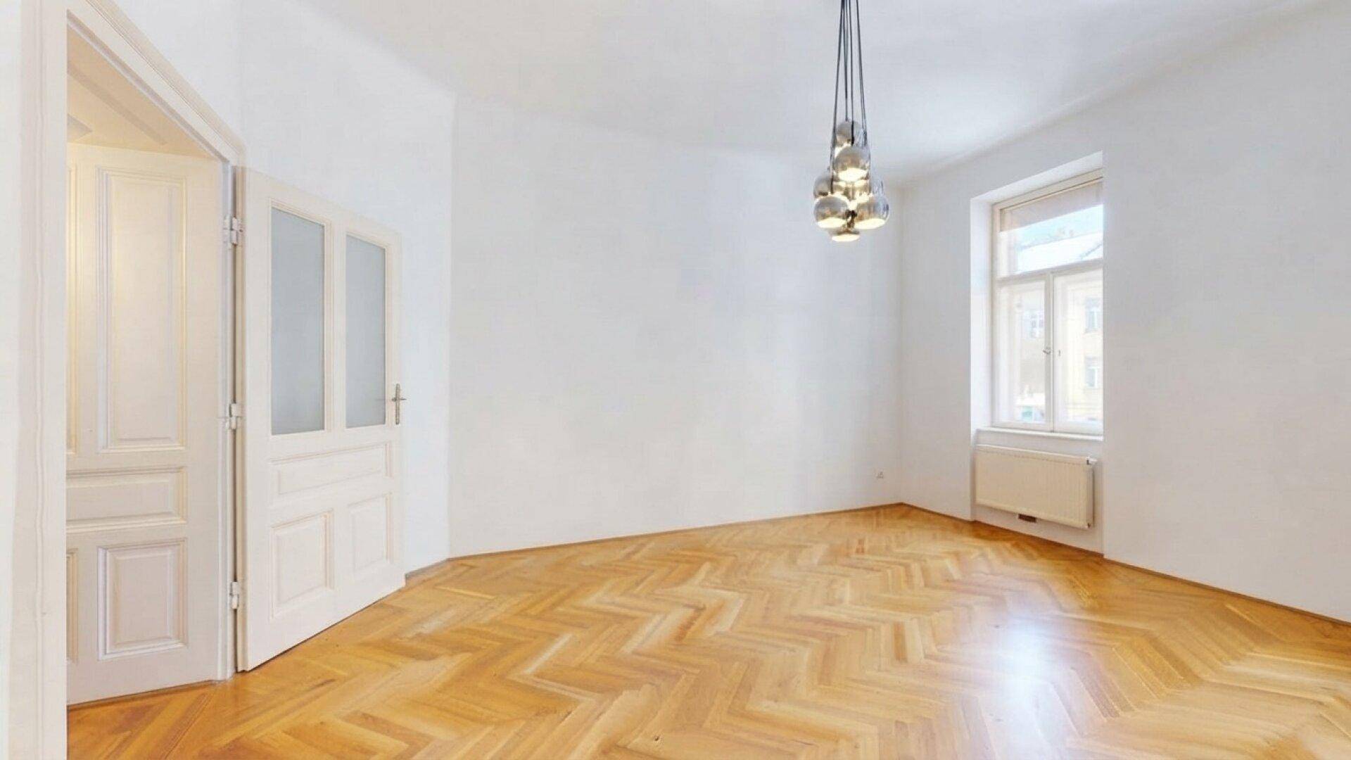 Helles Zimmer mit Fischgrätparkett, einem modernen Deckenlicht und einem Fenster mit Blick nach draußen.