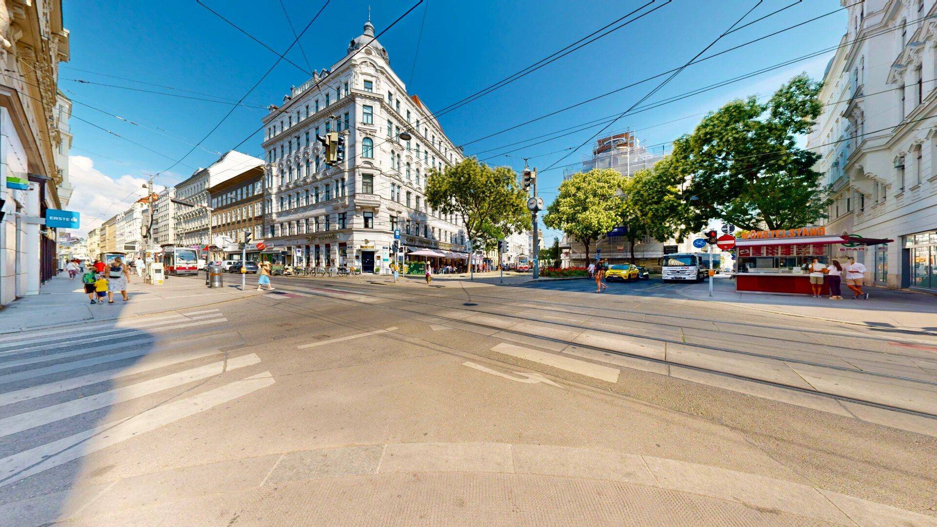 Weitläufige Straßenansicht einer belebten Stadtkreuzung mit historischen Gebäuden und öffentlichen Verkehrsmitteln.
