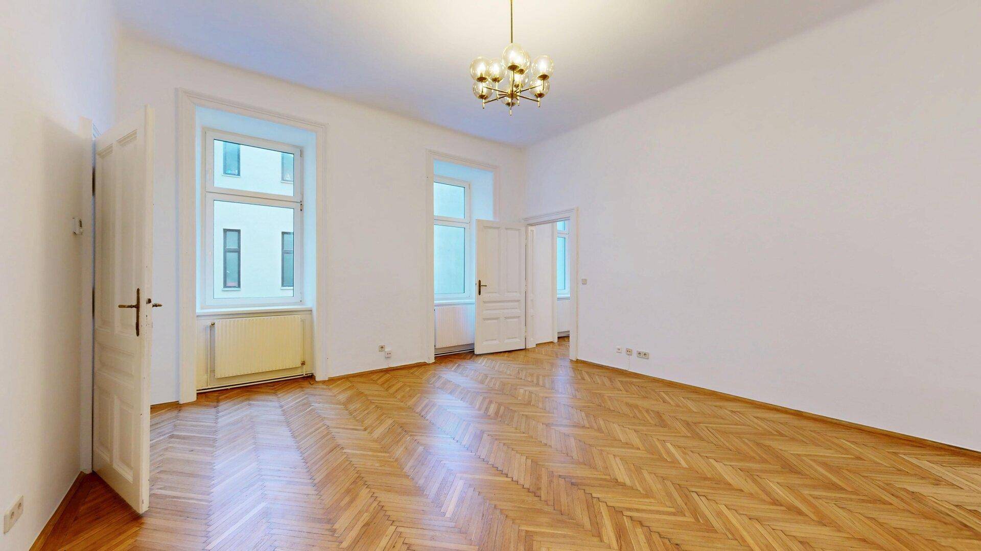 Helles Wohnzimmer mit klassischem Fischgrätparkett und einem eleganten Kronleuchter an der hohen Decke.