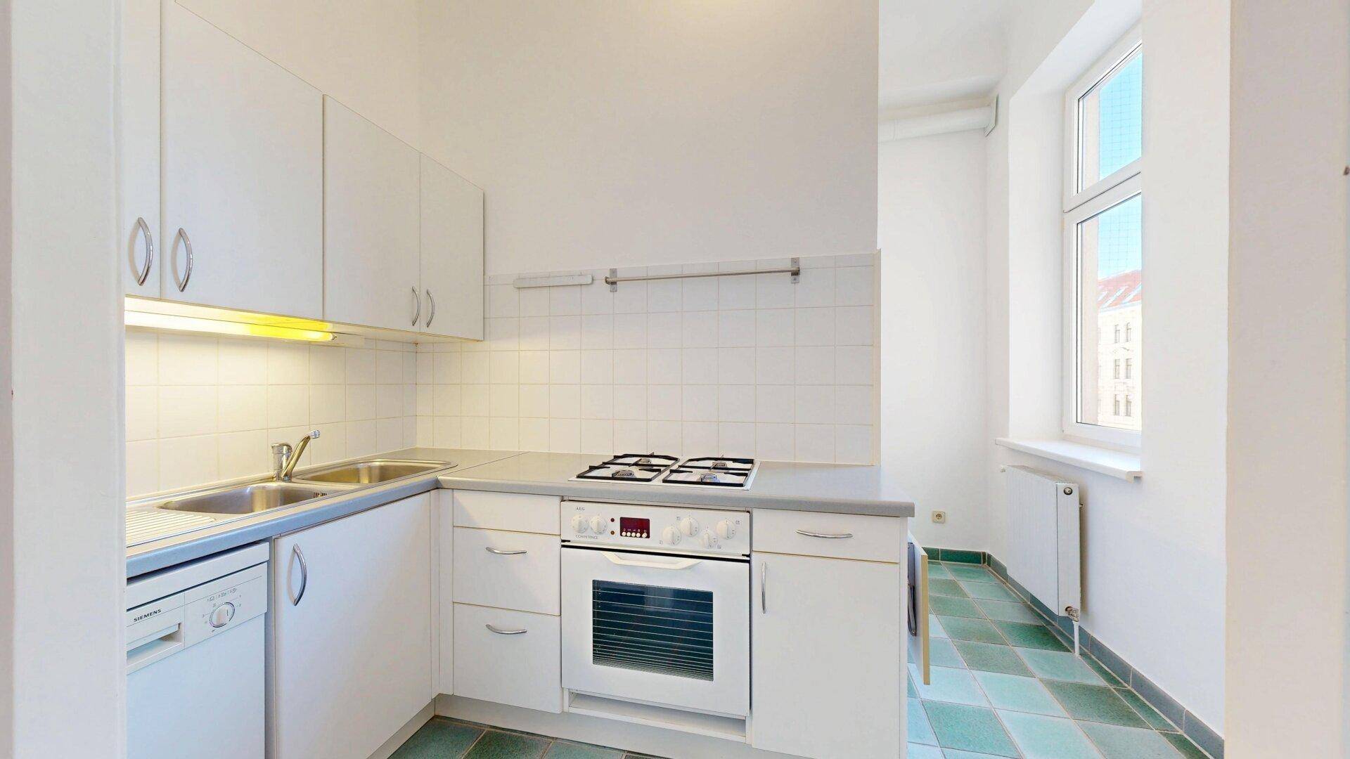 Funktionale Küche mit weißen Schränken, Gasherd, Backofen, Spülmaschine und einem Fenster.