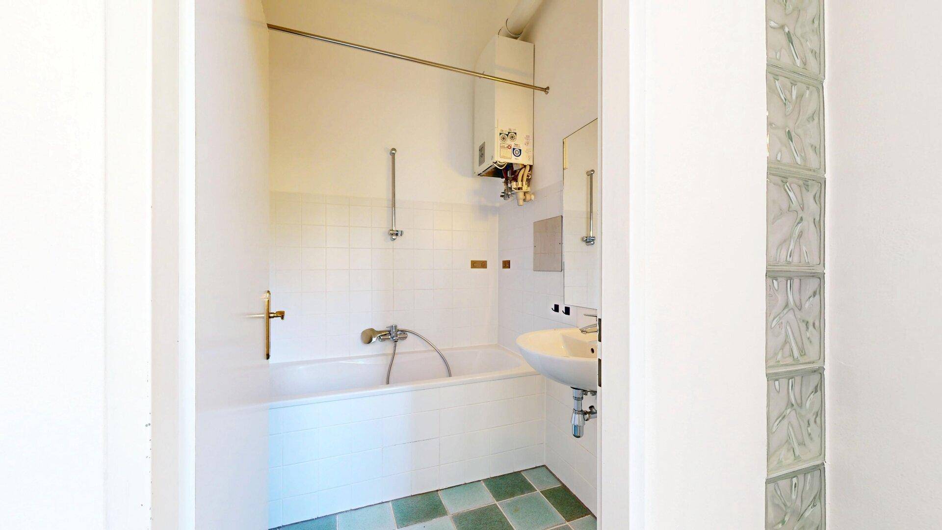 Badezimmer mit Badewanne, Waschbecken und einem Gasboiler, teilweise gefliest mit Glasbausteinen.