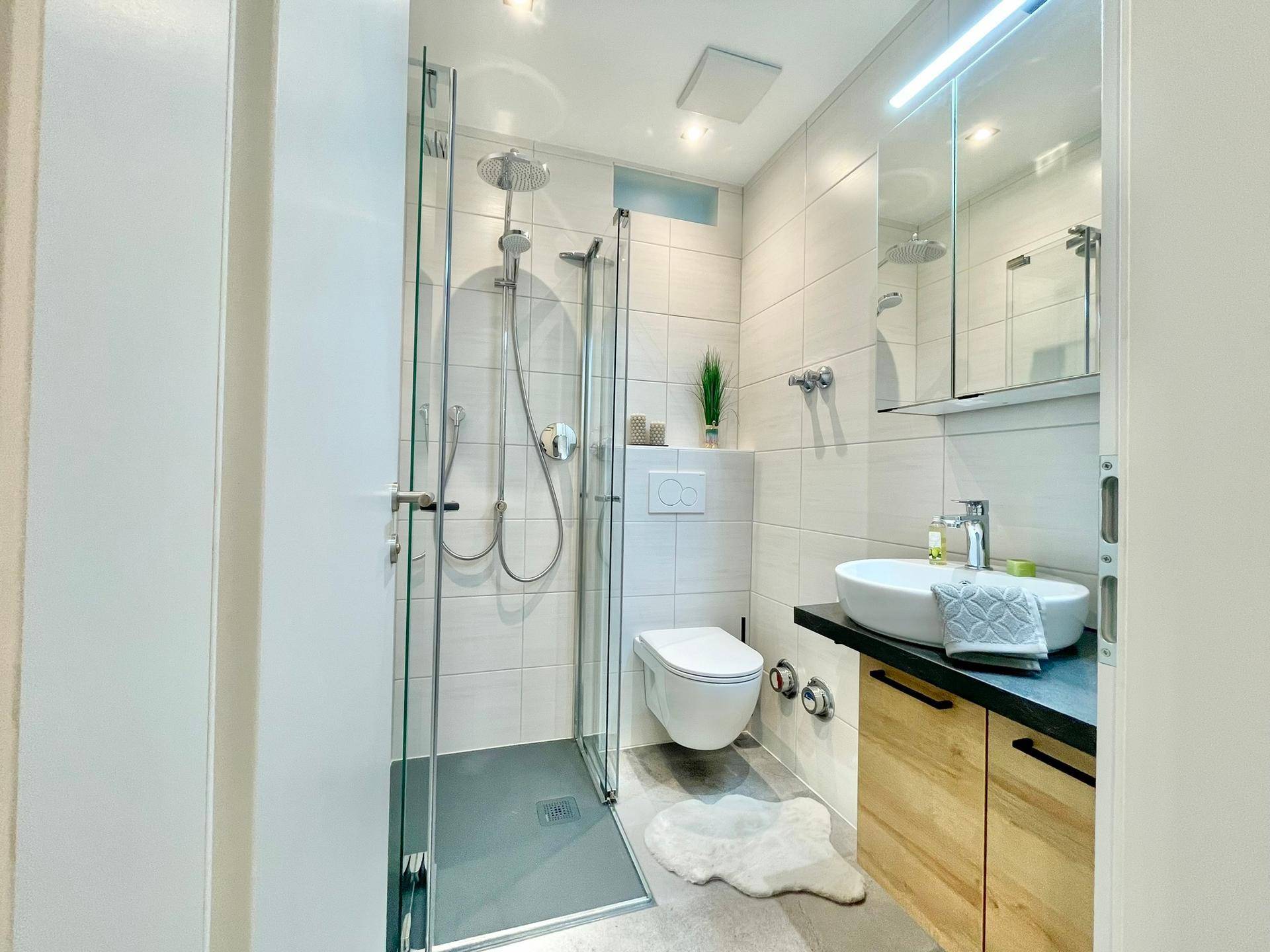 Modernes Badezimmer mit ebenerdiger Dusche, wandhängendem WC und stilvollem Waschbecken.