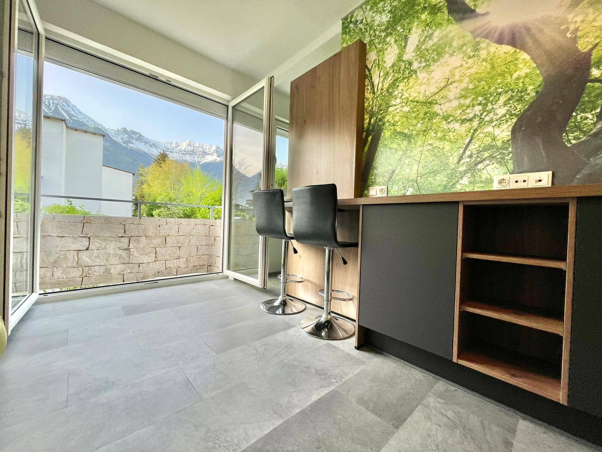 Heller Wohnbereich mit großen Fenstern, die einen beeindruckenden Bergblick und Zugang zum Balkon bieten.
