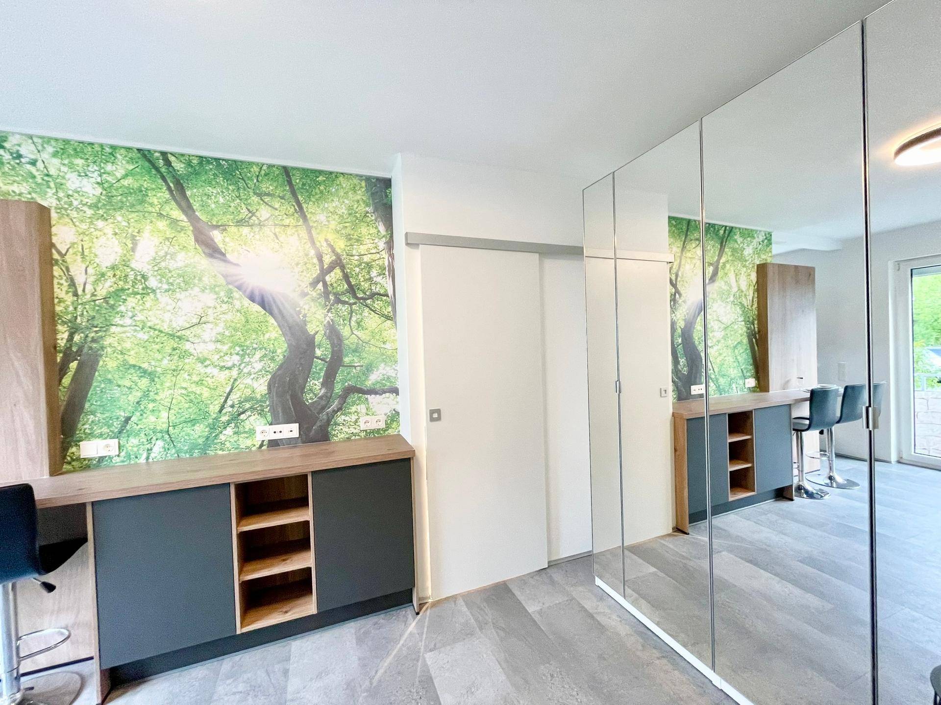 Moderner Wohnbereich mit Natur-Wandtapete, Spiegelschränken und Schiebetür, die den Raum optisch vergrößern.